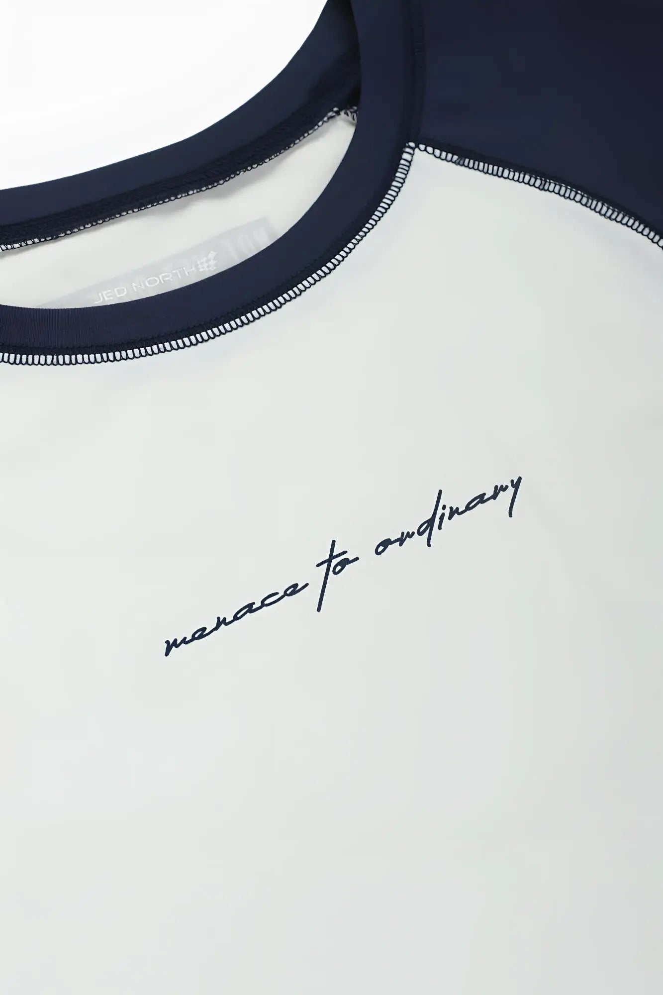 White and navy blue raglan sleeveless muscle tank with black cursive embroidery manace to ordinary on chest