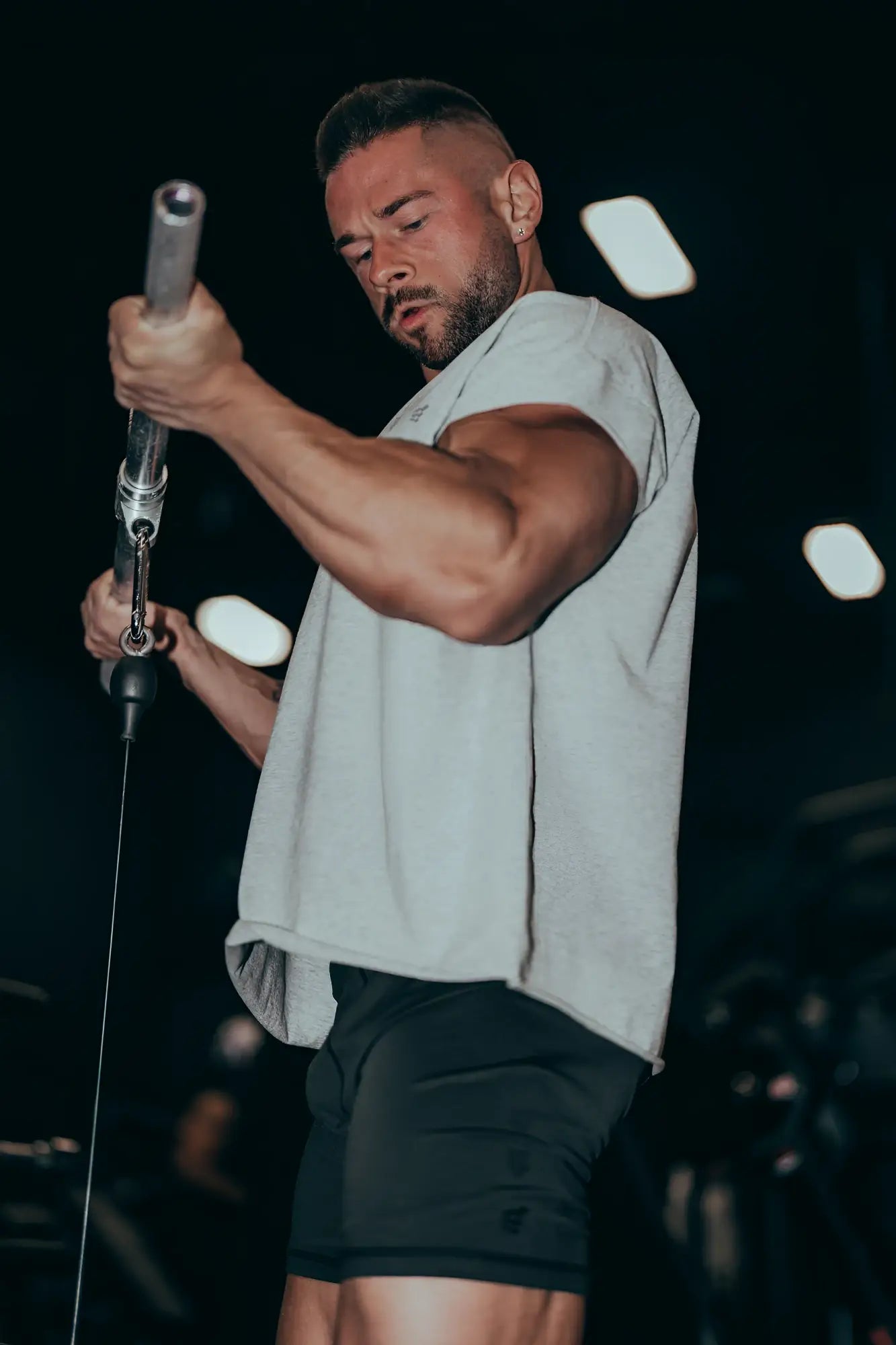 A man wearing black retro bodybuilding shorts in lightweight fabric holds a silver cable machine handle during workout