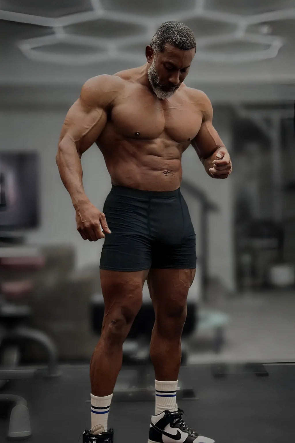A muscular man wearing black retro bodybuilding shorts with white socks and black-and-white Nike sneakers