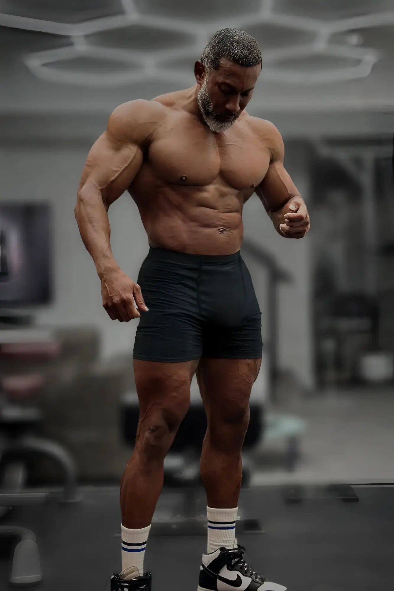 A muscular man wearing black retro bodybuilding shorts with white socks and black-and-white Nike sneakers