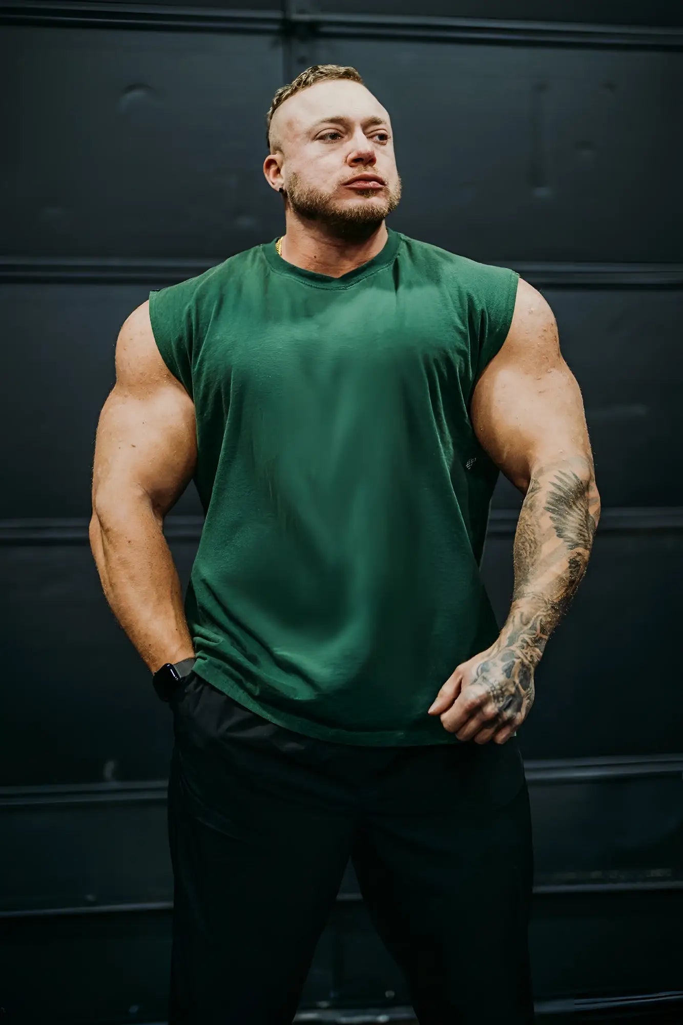A man wearing a dark green retro oversized muscle tee sleeveless athletic shirt paired with black pants