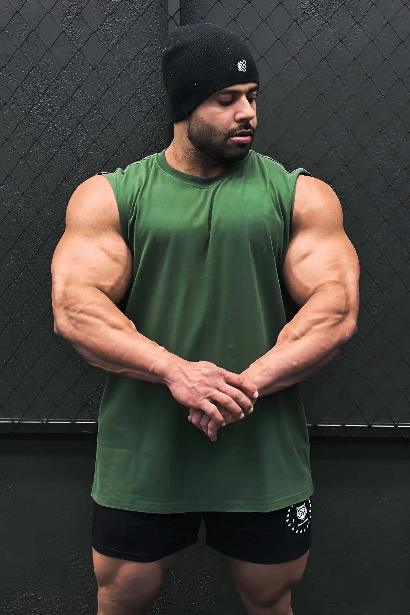 A muscular man wearing a forest green retro oversized muscle tee and black athletic shorts with a white logo