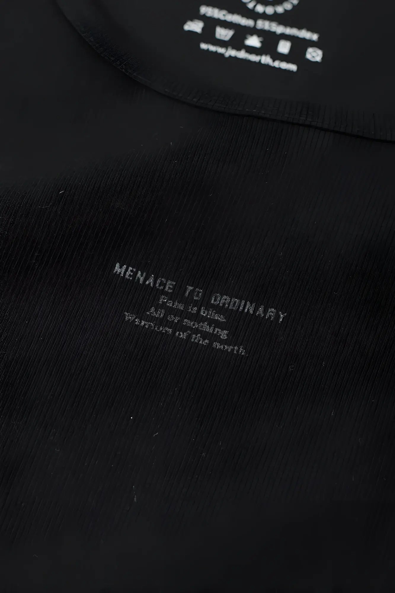 Black ribbed muscle tank top with white menace to ordinary text and care instructions inside collar