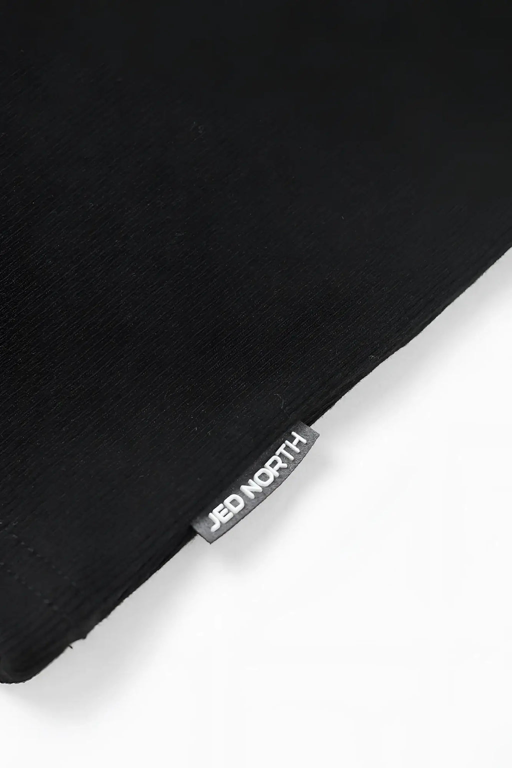 Black ribbed muscle tank top featuring a small rectangular jed north brand tag stitched on the corner