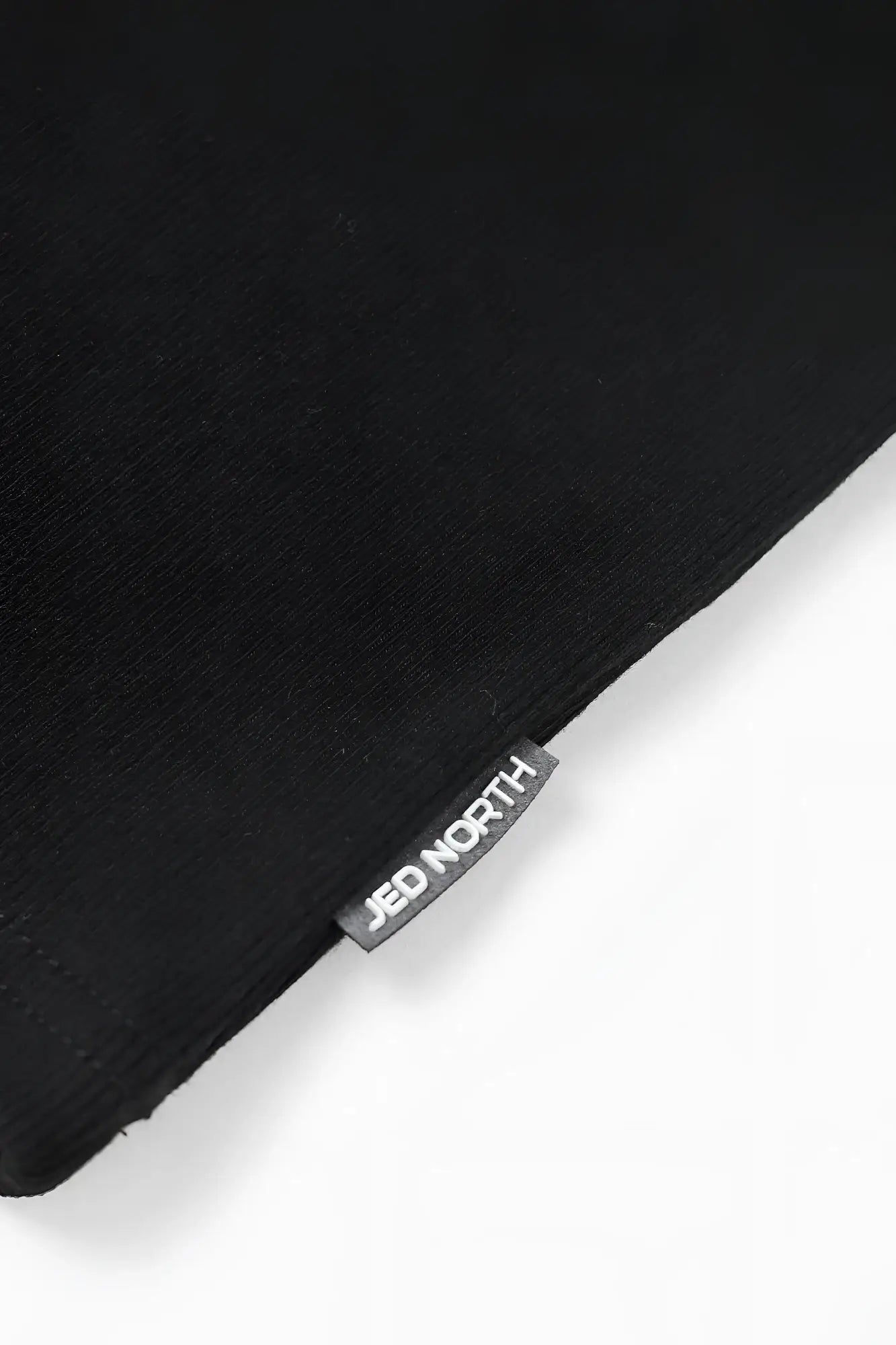 Black ribbed muscle tank top featuring a small rectangular jed north brand tag stitched on the corner