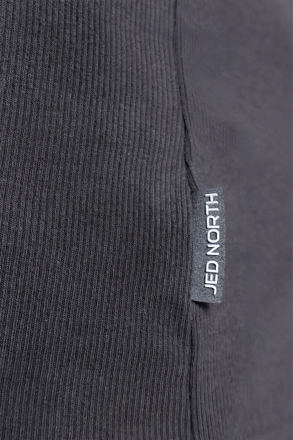 Dark gray ribbed knit fabric with a small rectangular jed north tag on the ribbed muscle tank top seam