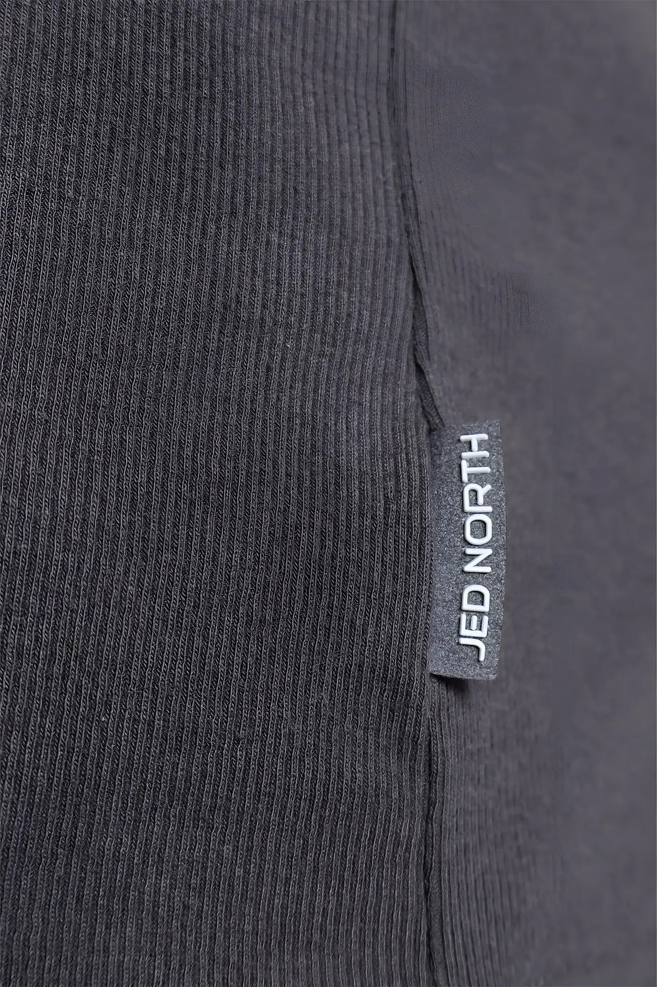 Dark gray ribbed knit fabric with a small rectangular jed north tag on the ribbed muscle tank top seam