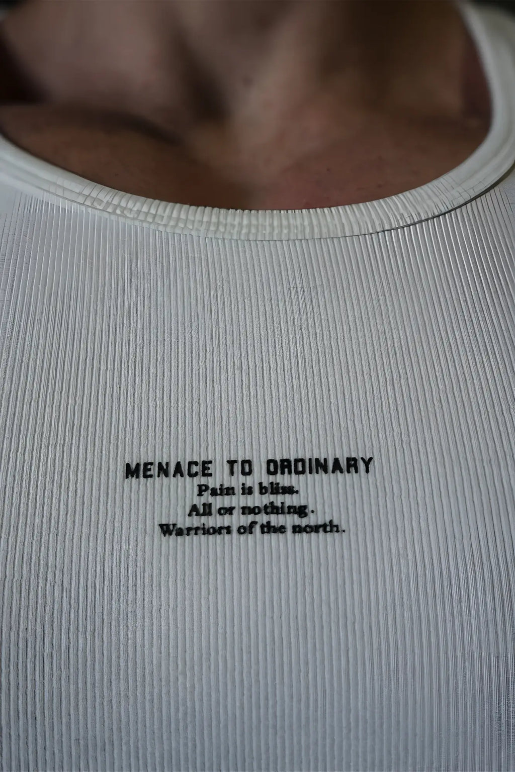 White ribbed muscle tank top with black text reading menace to ordinary and pain is bliss on front