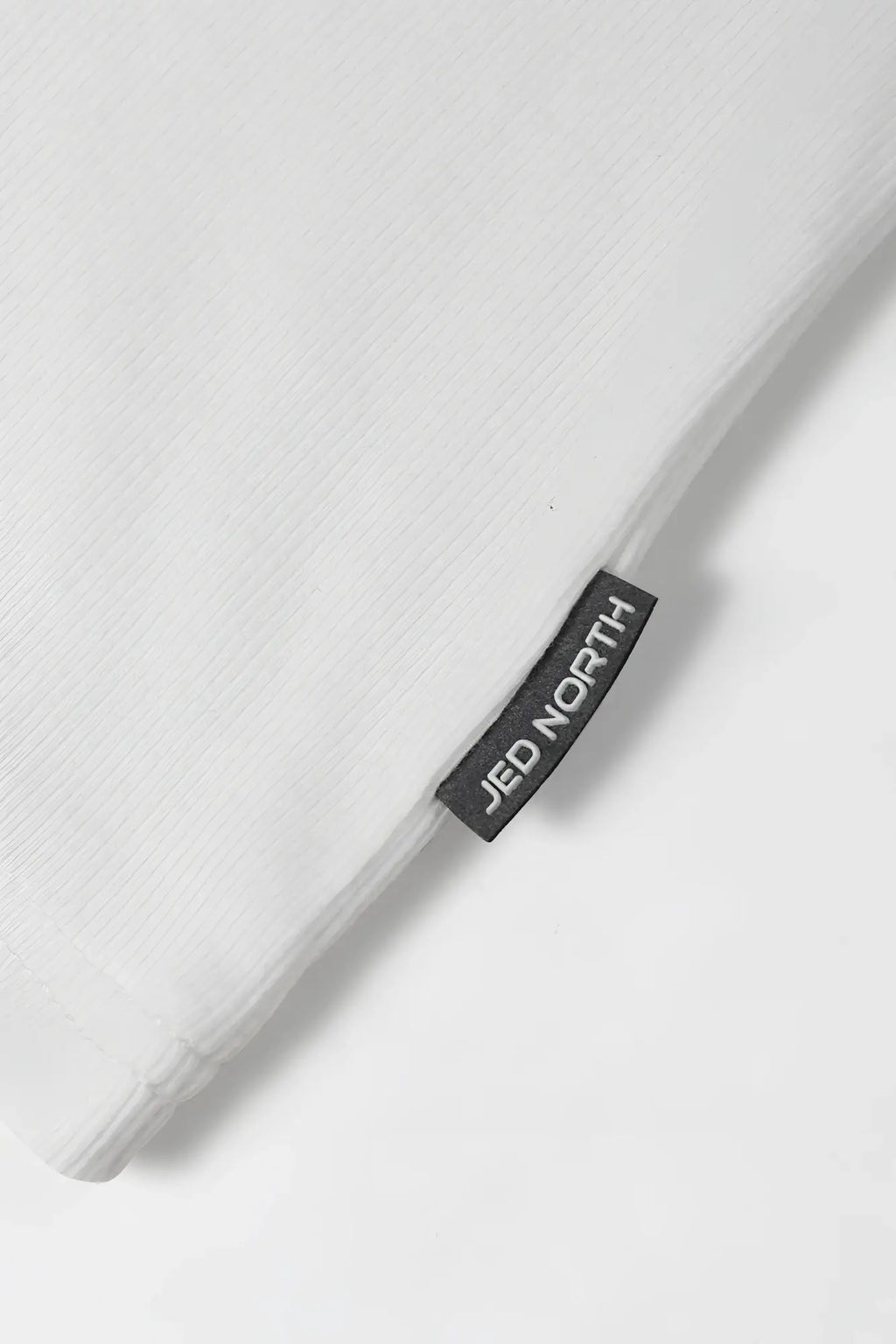 White ribbed muscle tank top with a white linen pillowcase featuring a black jed north brand tag