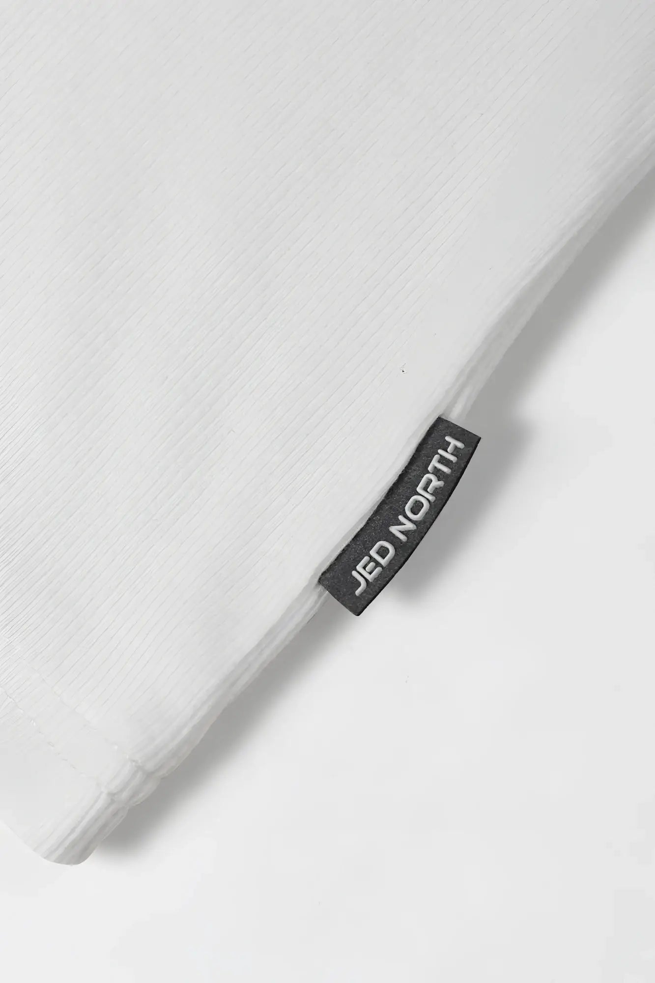 White ribbed muscle tank top with a white linen pillowcase featuring a black jed north brand tag