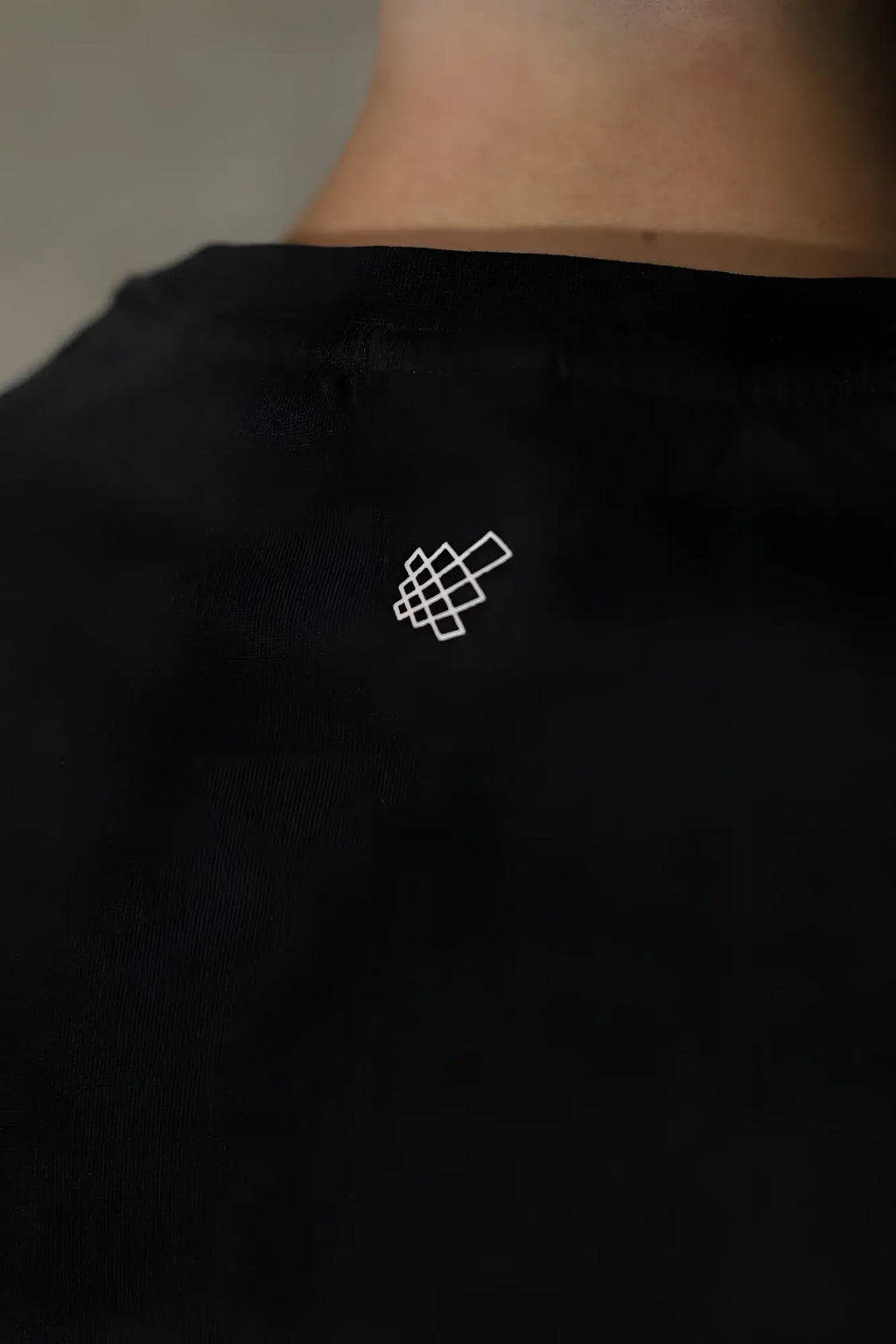 Back view of black jed north sleeveless box cut tank top with a small white geometric logo on the back
