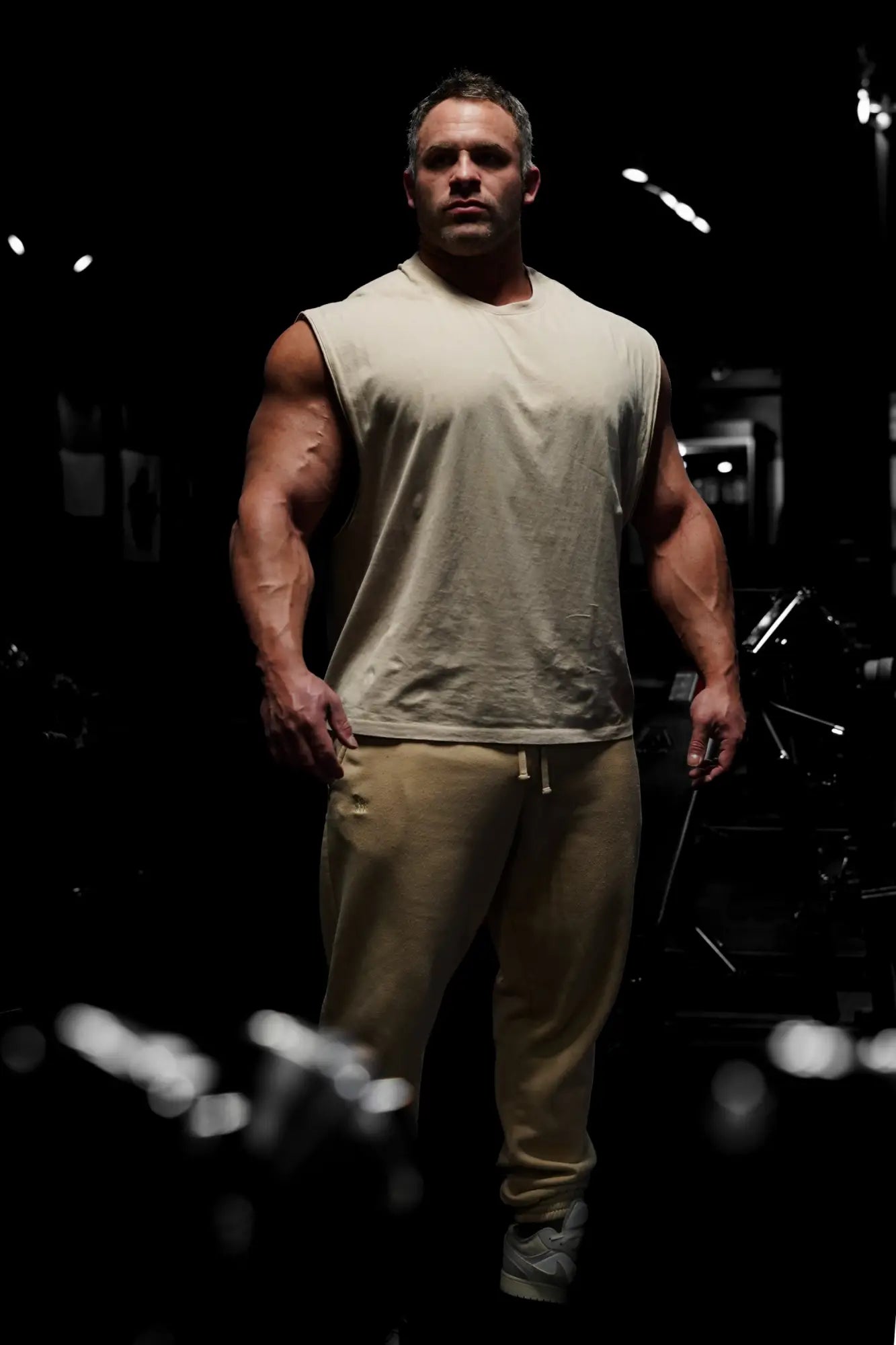 A muscular man wearing jed north sleeveless box cut tank top in light khaki with matching khaki sweatpants