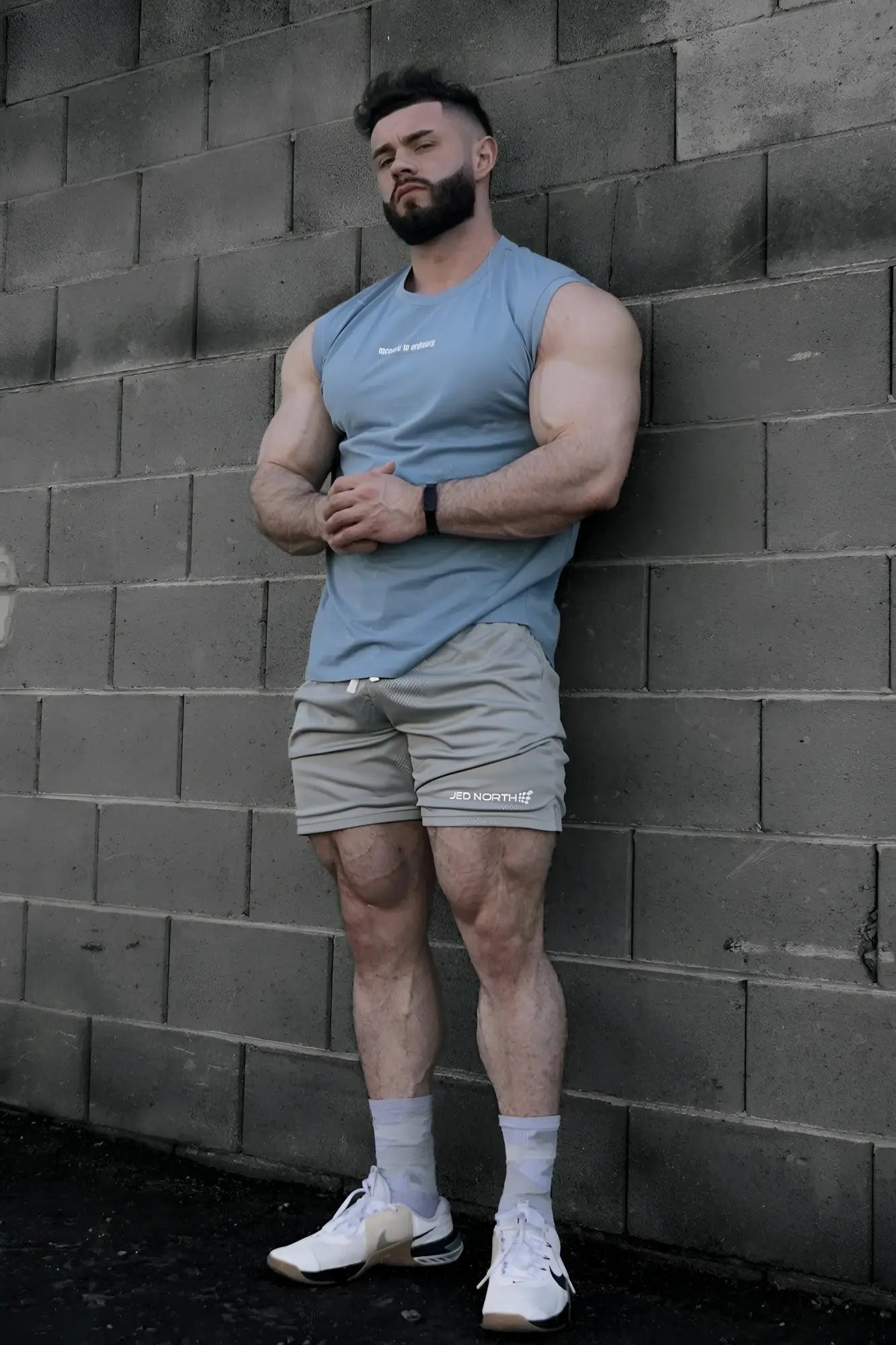 A man wearing a Jed North light blue sleeveless muscle tee and gray shorts with jersey north logo on left leg