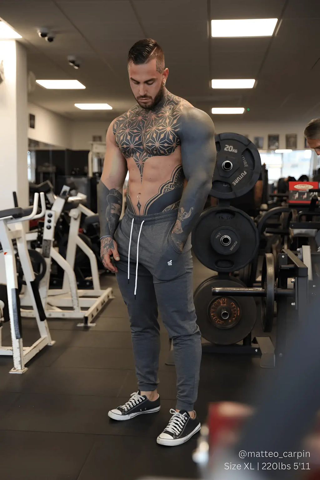 Gray spirit joggers with white drawstrings and small left thigh logo worn by tattooed man in gym setting