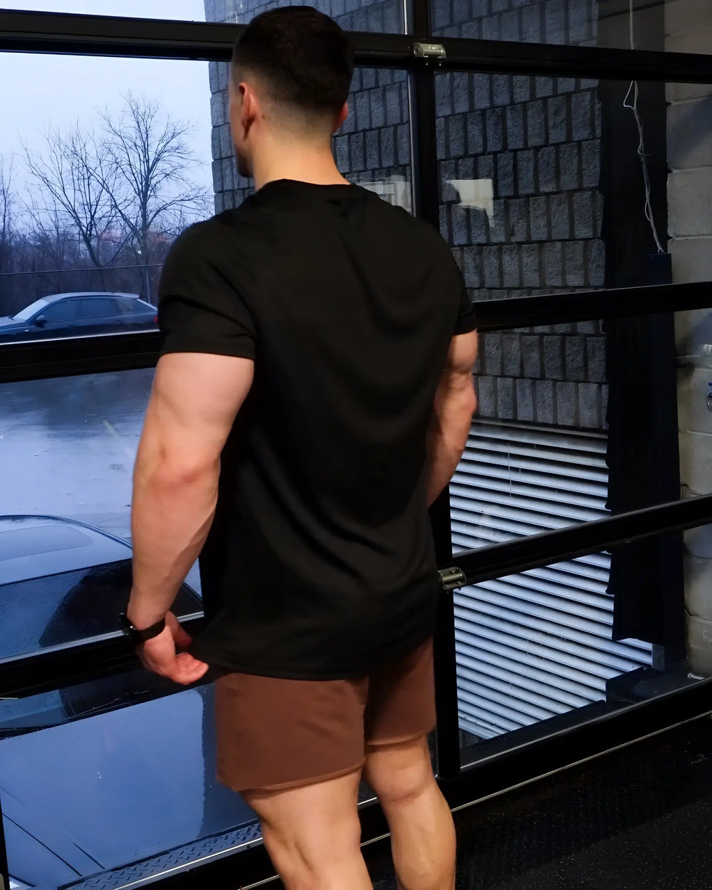A man wearing the back of a jed north tactical fast-dry training t-shirt in obsidian black stands by a window