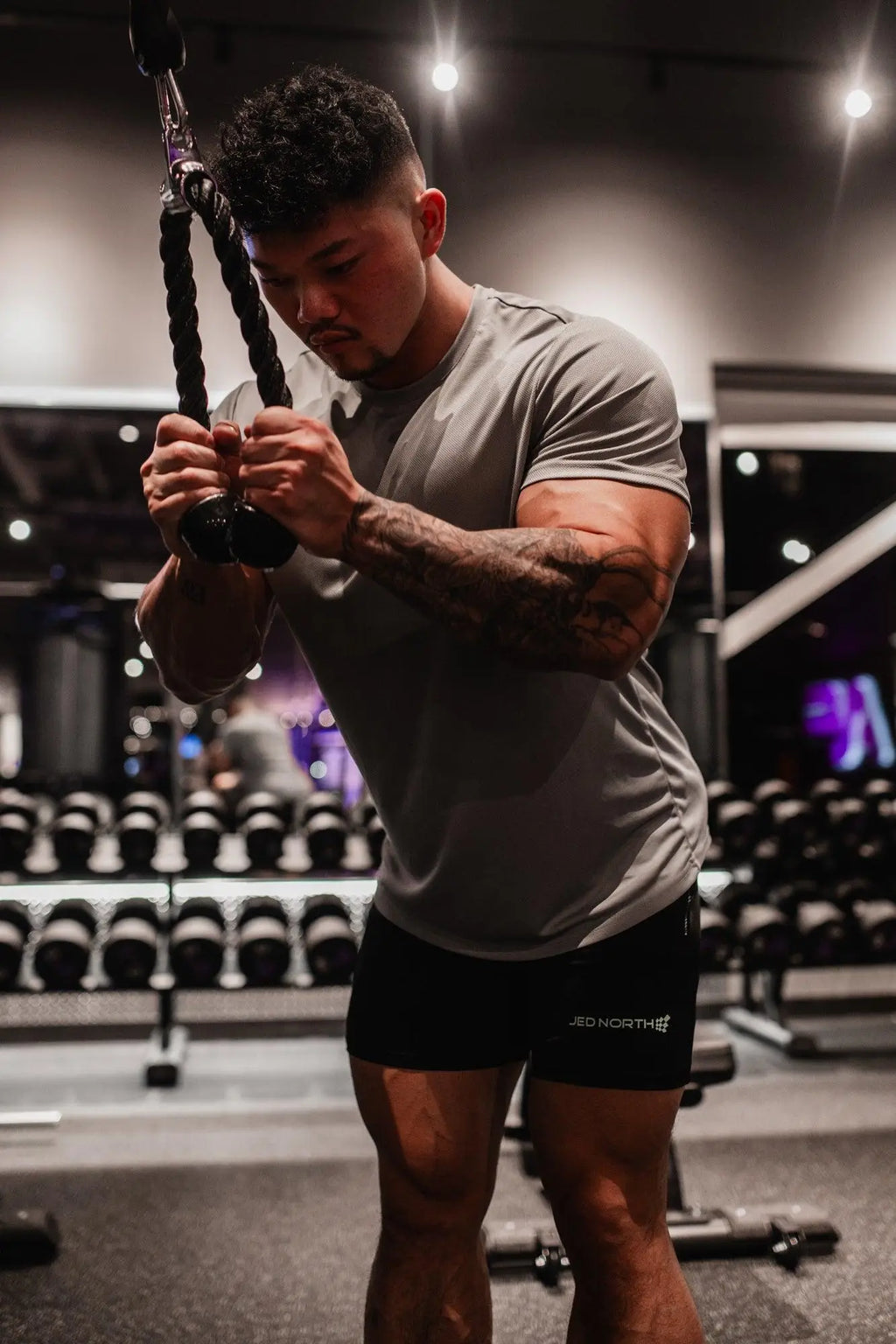 A man with tattoos wearing a jed north tactical fast-dry training t-shirt in polar silver holding resistance ropes in gym