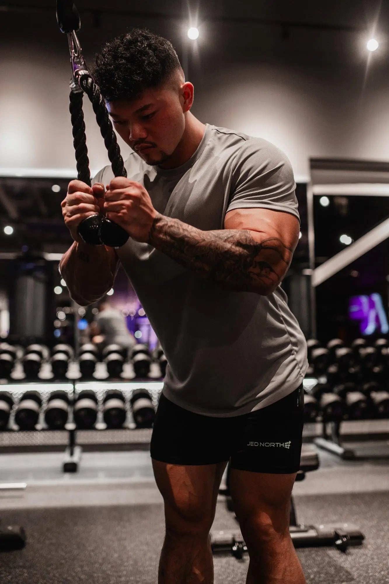 A man with tattoos wearing a jed north tactical fast-dry training t-shirt in polar silver holding resistance ropes in gym