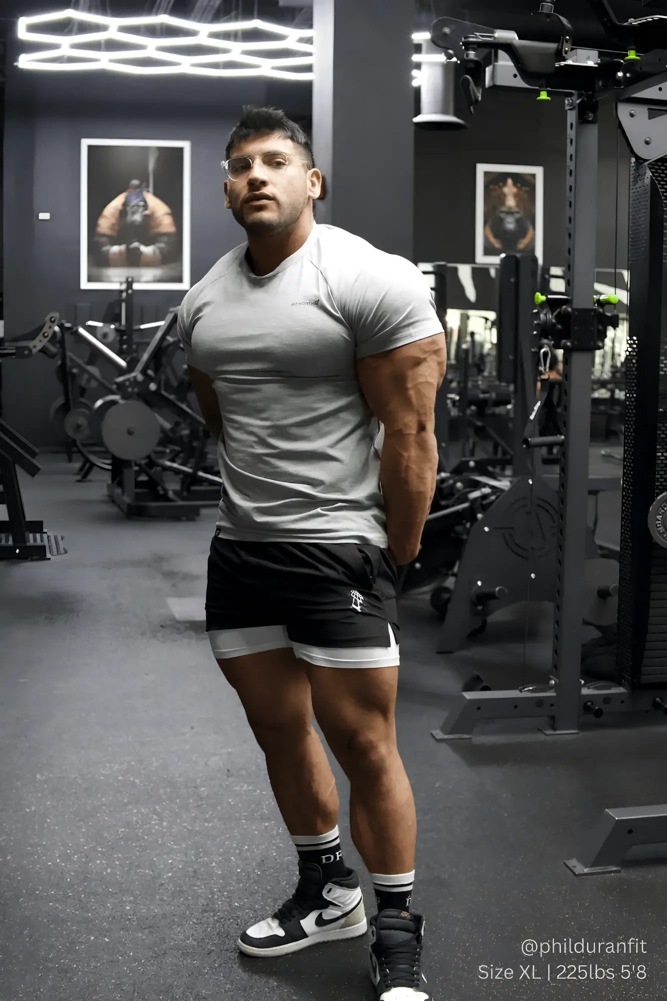 A muscular man wearing a heather gray jed north titan 2.0 muscle fit t shirt with black shorts and white trim