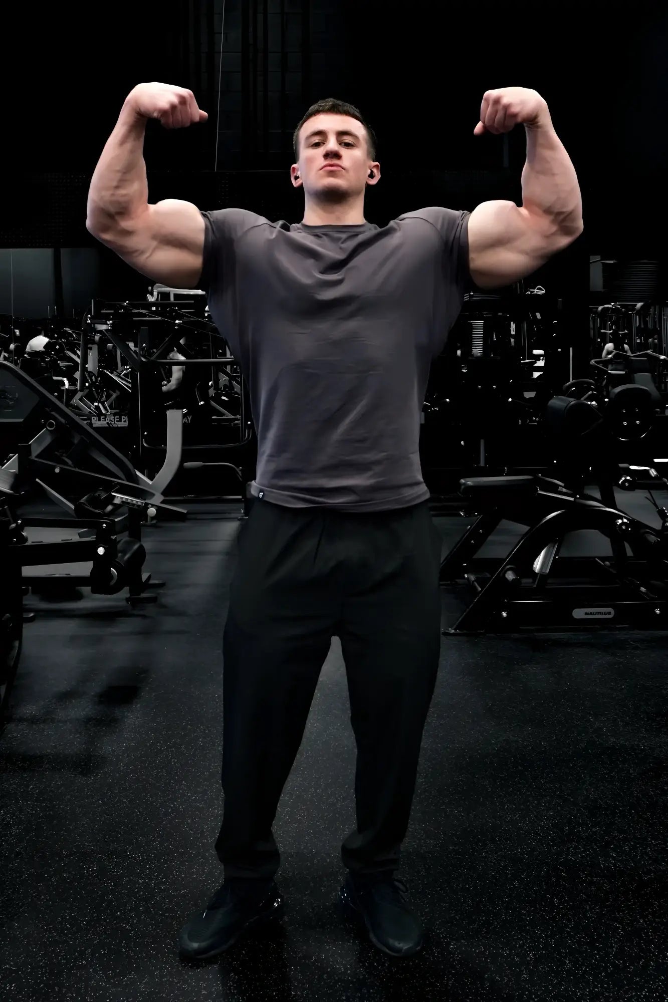 A muscular man wearing a taupe jed north titan 2.0 muscle-fit short-sleeved t-shirt flexes in a gym setting