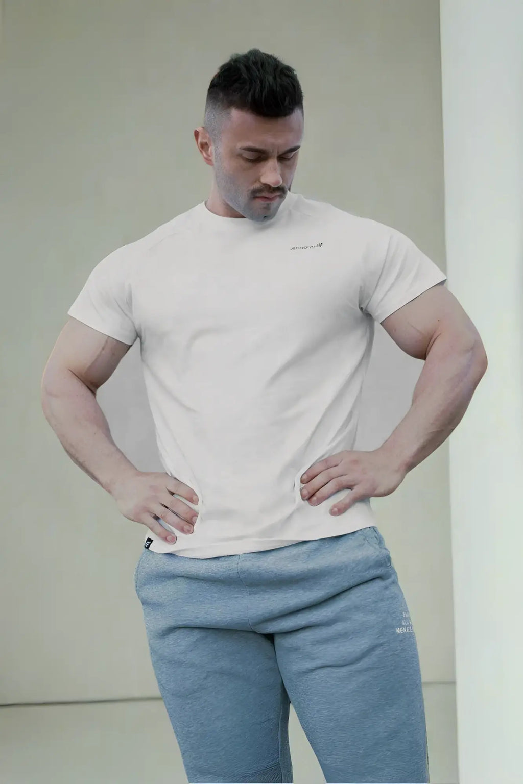 A man wearing a white jed north titan 2.0 muscle-fit t-shirt with a small chest logo and light blue athletic pants