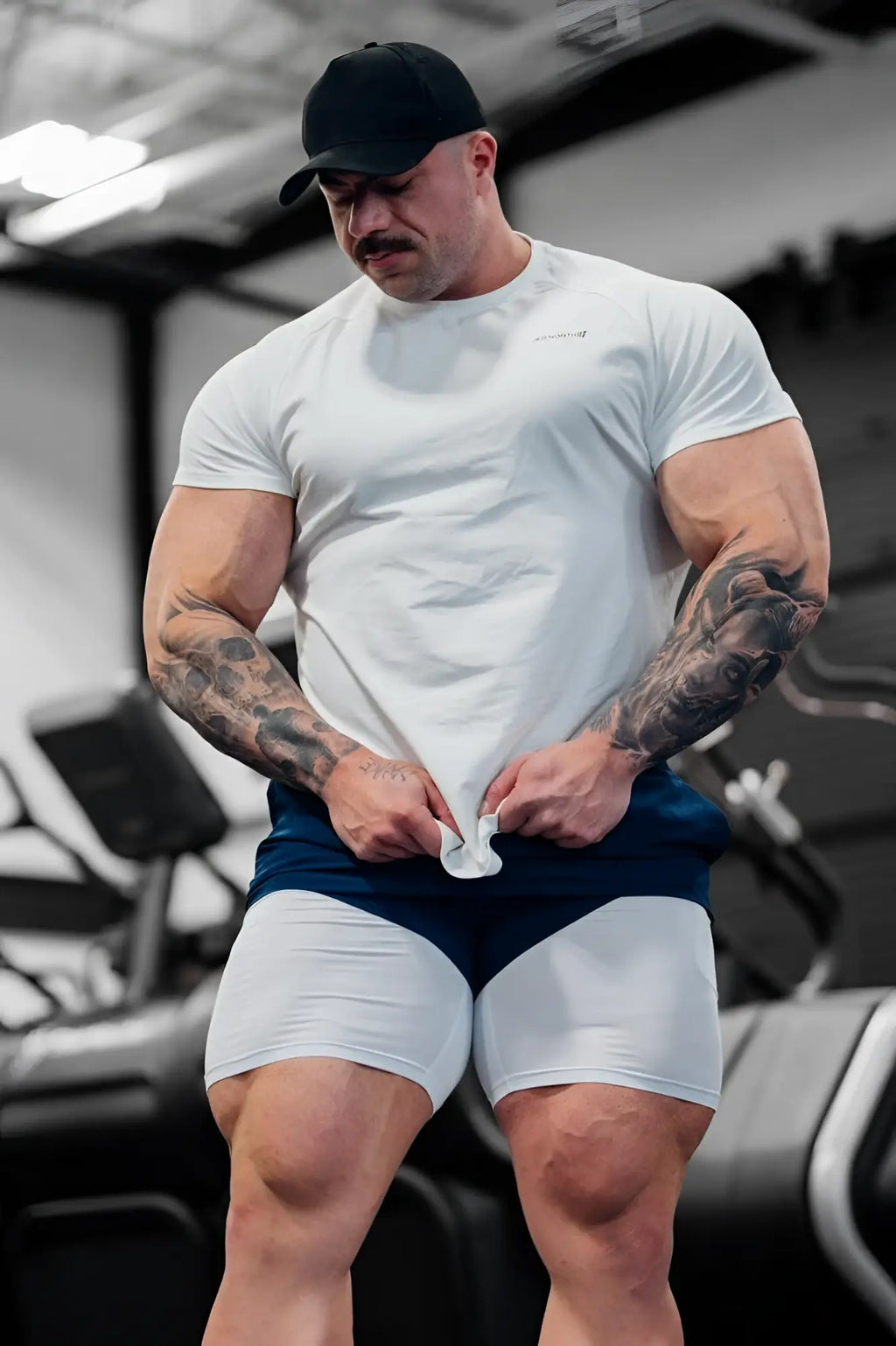 A muscular man wearing a white Jed North Titan 2.0 muscle-fit t-shirt made of breathable fabric with navy blue athletic shorts