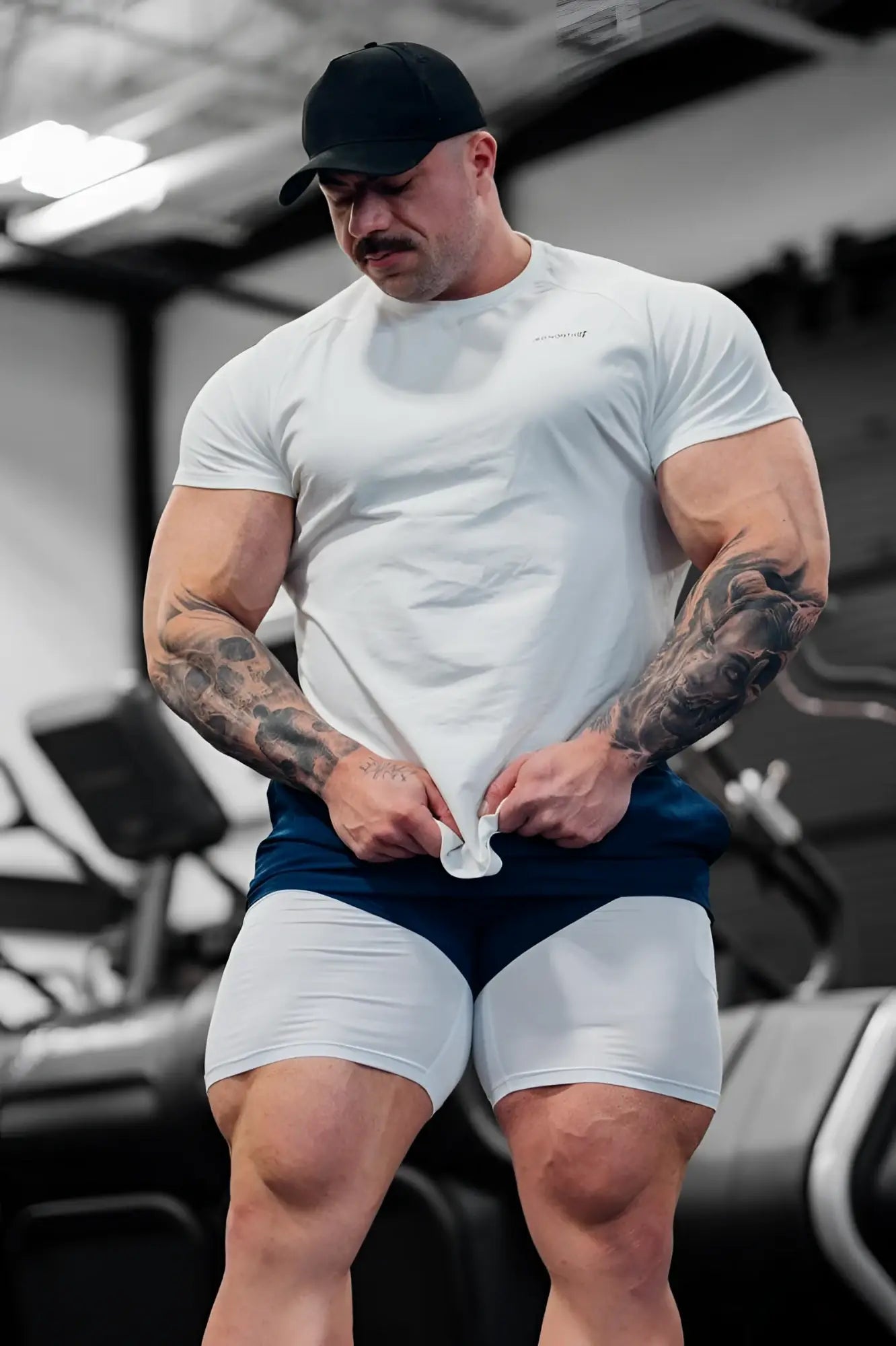 A muscular man wearing a white Jed North Titan 2.0 muscle-fit t-shirt made of breathable fabric with navy blue athletic shorts