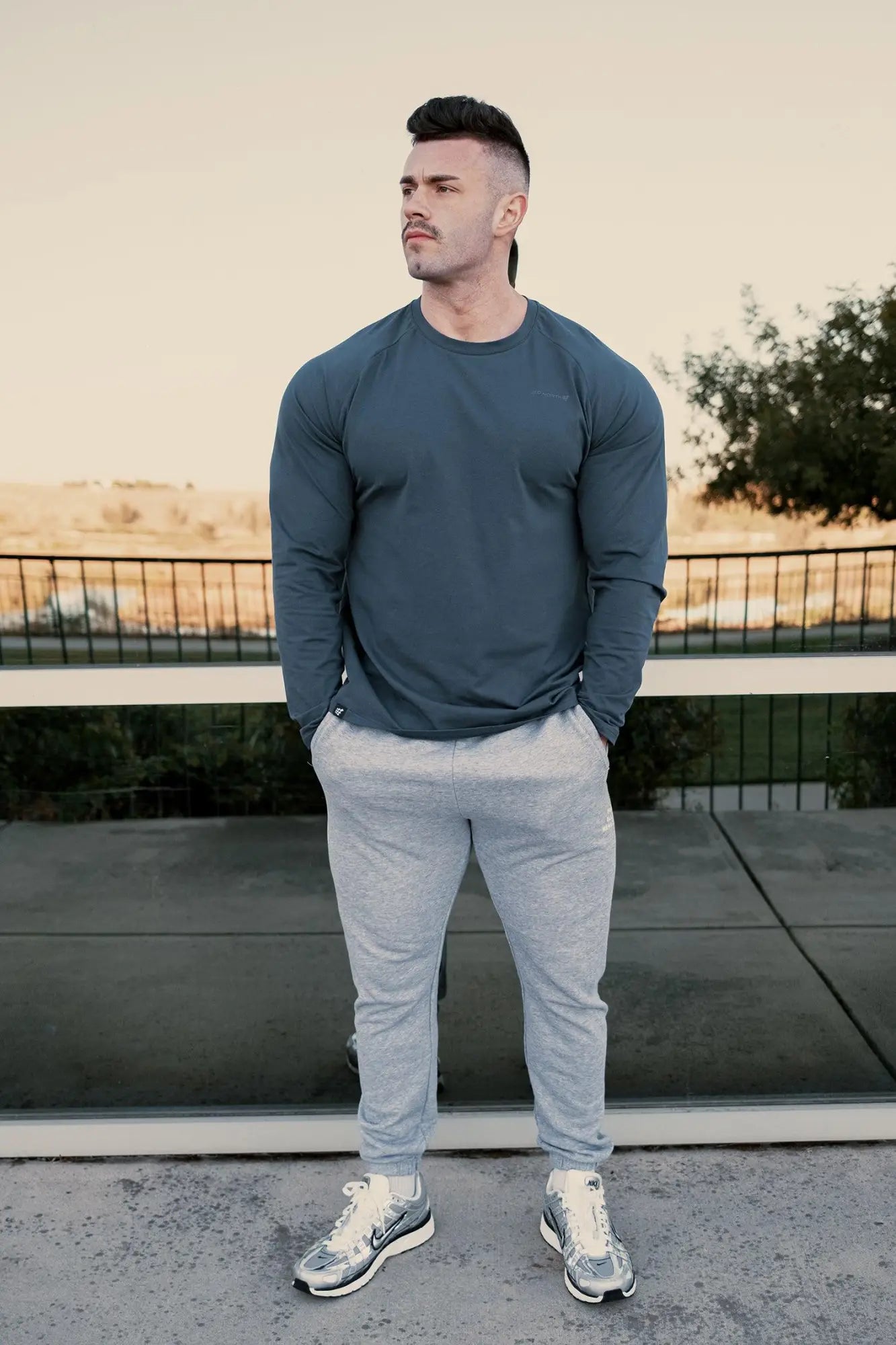 A man wearing a jed north titan muscle-fit long sleeve t-shirt in steel blue paired with light gray joggers