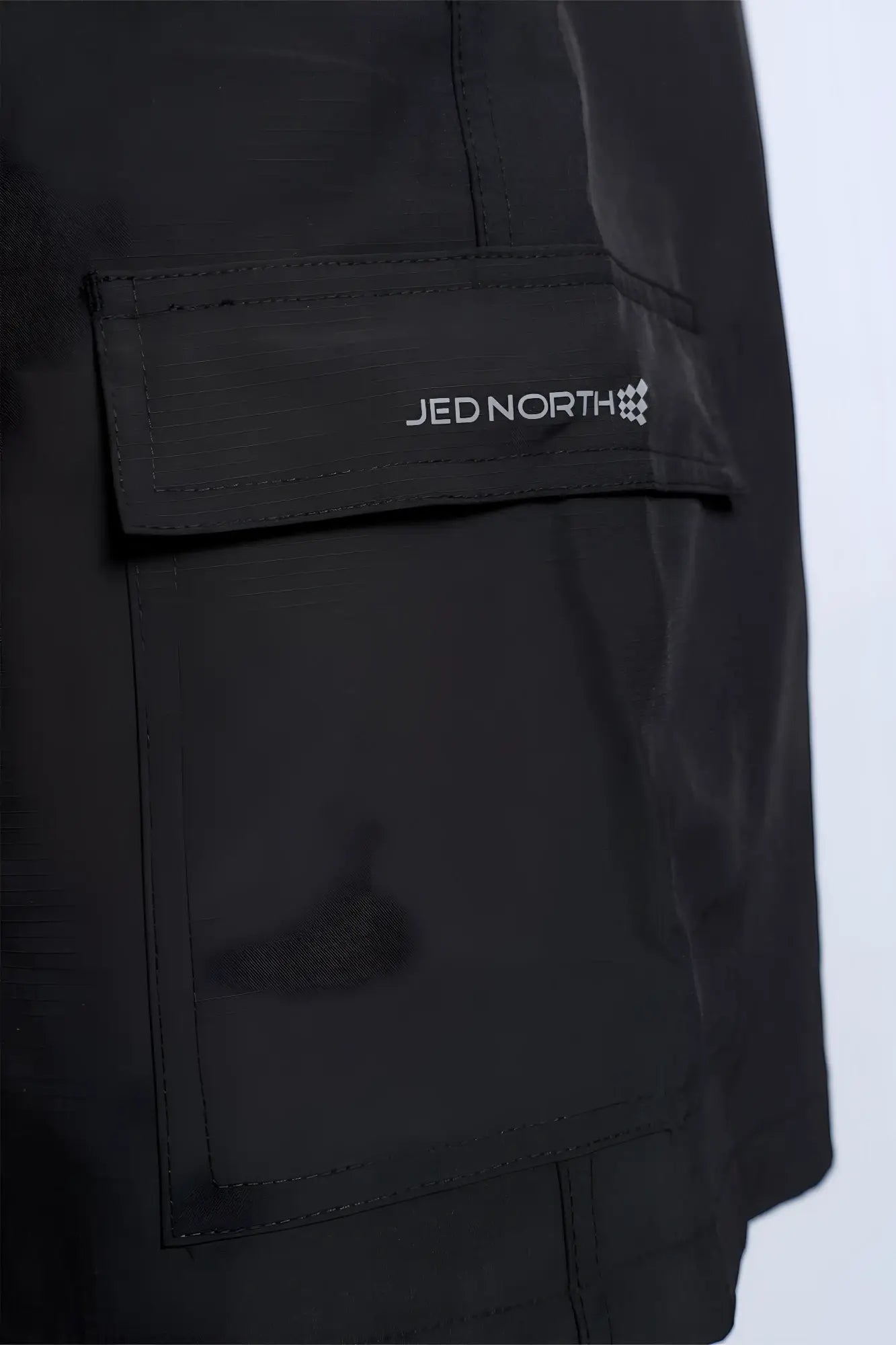 Black trek 4.5 cargo shorts made of sleek durable fabric with subtle sheen and jed north branded patch in white lettering