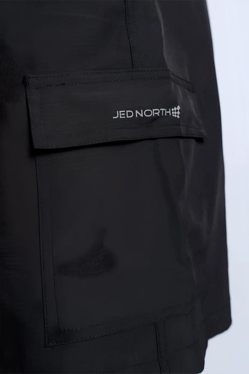 Black trek 4.5 cargo shorts made of sleek durable fabric with subtle sheen and jed north branded patch in white lettering