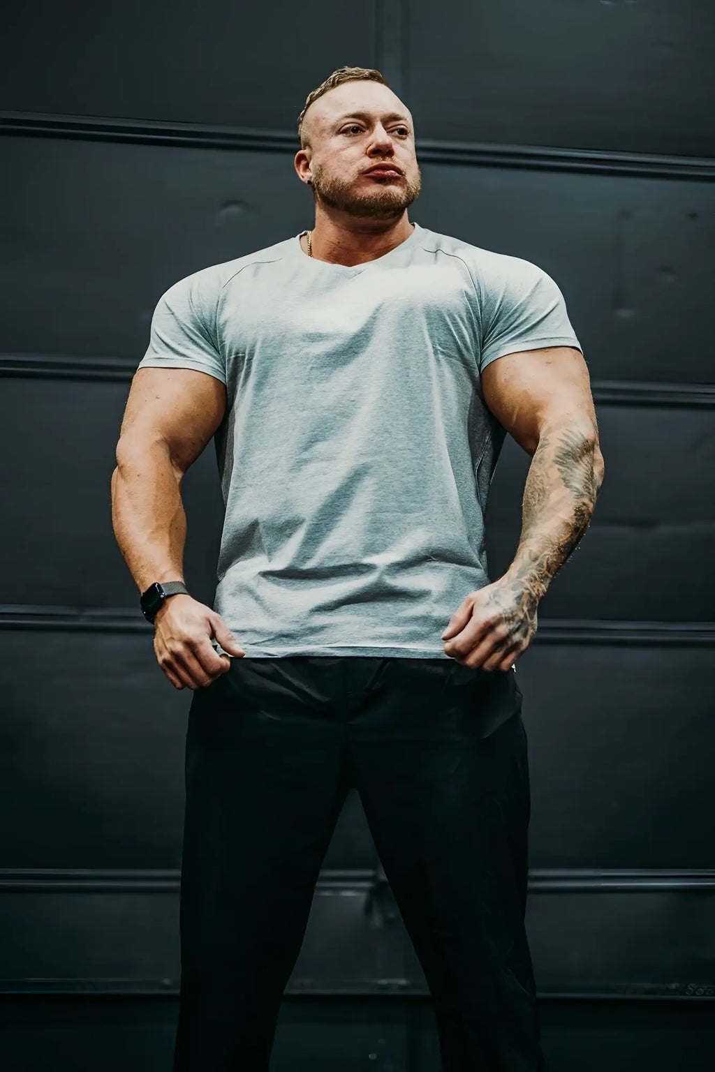 A man wearing a light gray v neck muscle-fit t-shirt with a subtle heathered texture and black athletic pants