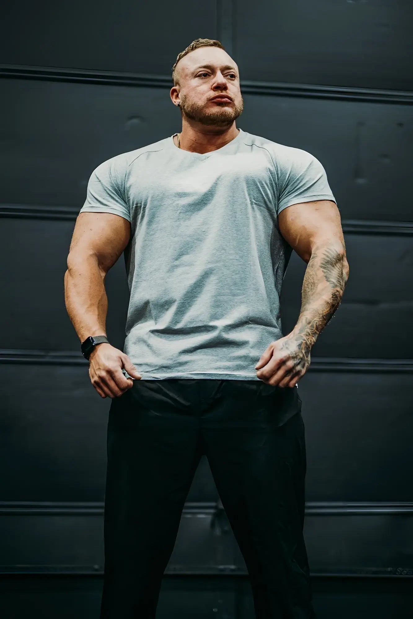 A man wearing a light gray v neck muscle-fit t-shirt with a subtle heathered texture and black athletic pants