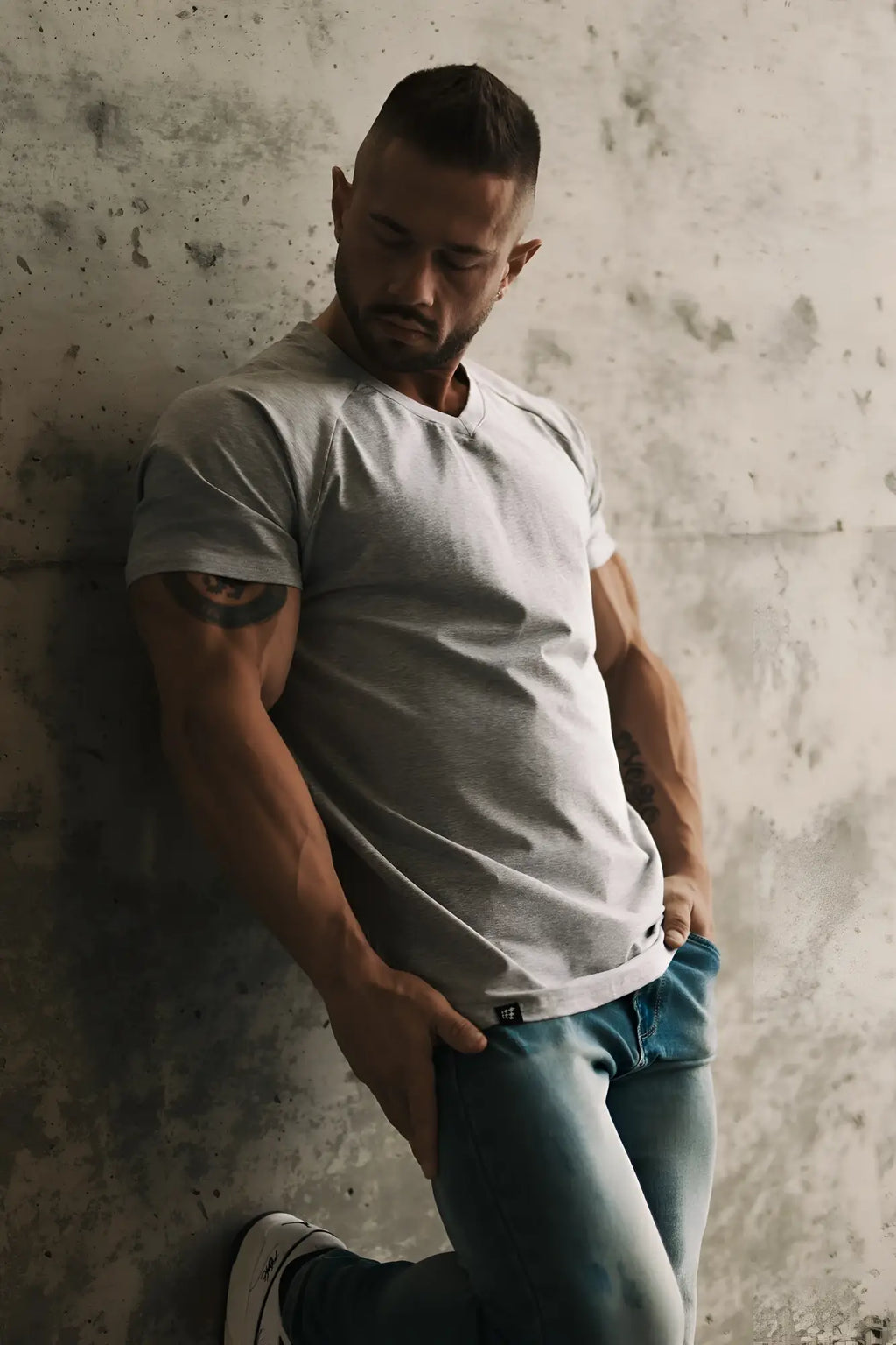 A man wearing a light gray short-sleeved muscle-fit crew neck t-shirt with visible stitching and a small lower logo
