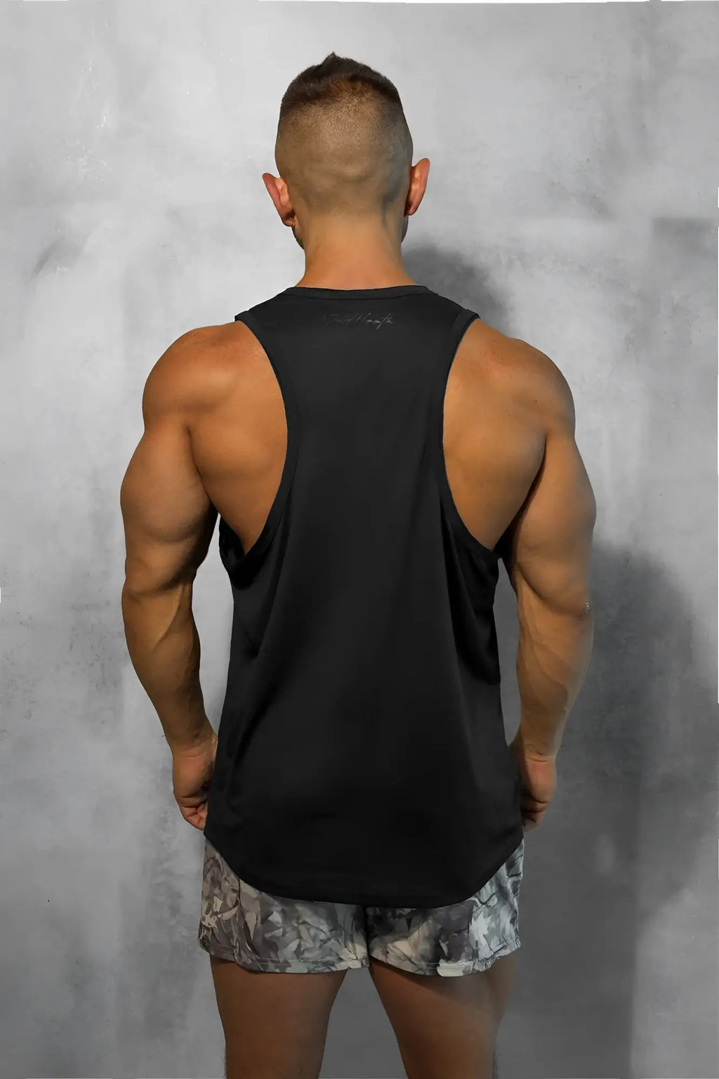 Back view of vital raw-hem tank top 2.0 black muscle tank with racerback design and subtle brand logo on upper back