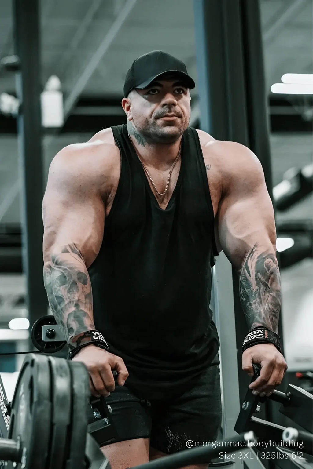 A muscular man wearing a black Vital Raw-Hem Tank Top 2.0 with detailed arm tattoos and a cap
