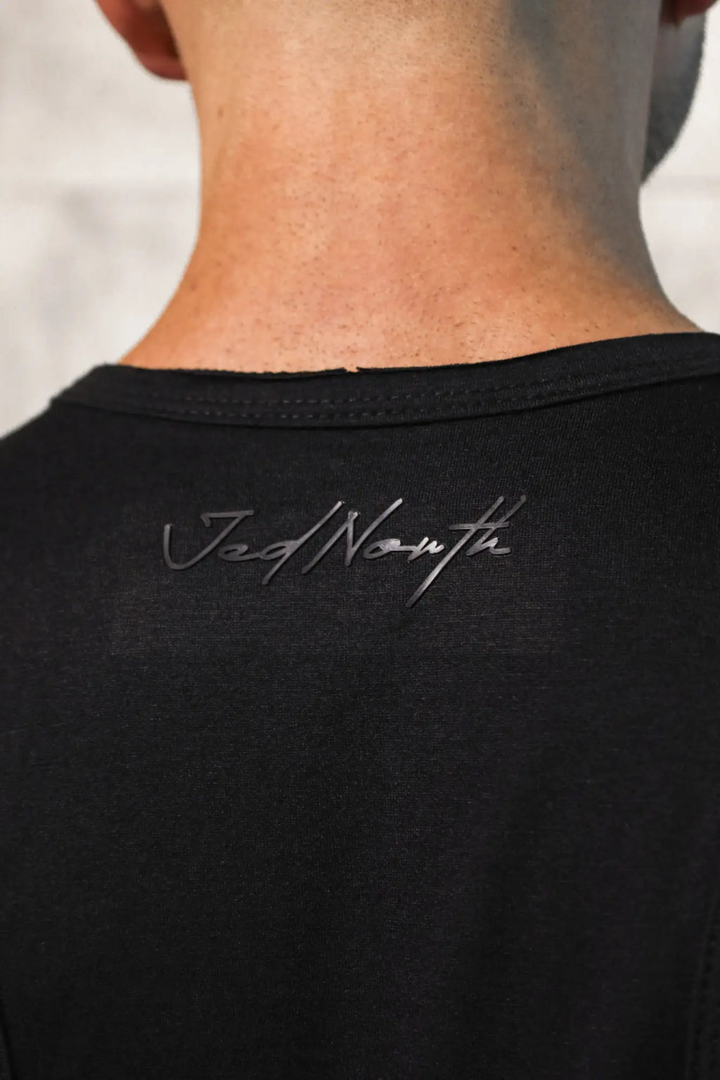 Black vital raw-hem tank top 2.0 showing back with silver cursive jad north logo on cotton fabric