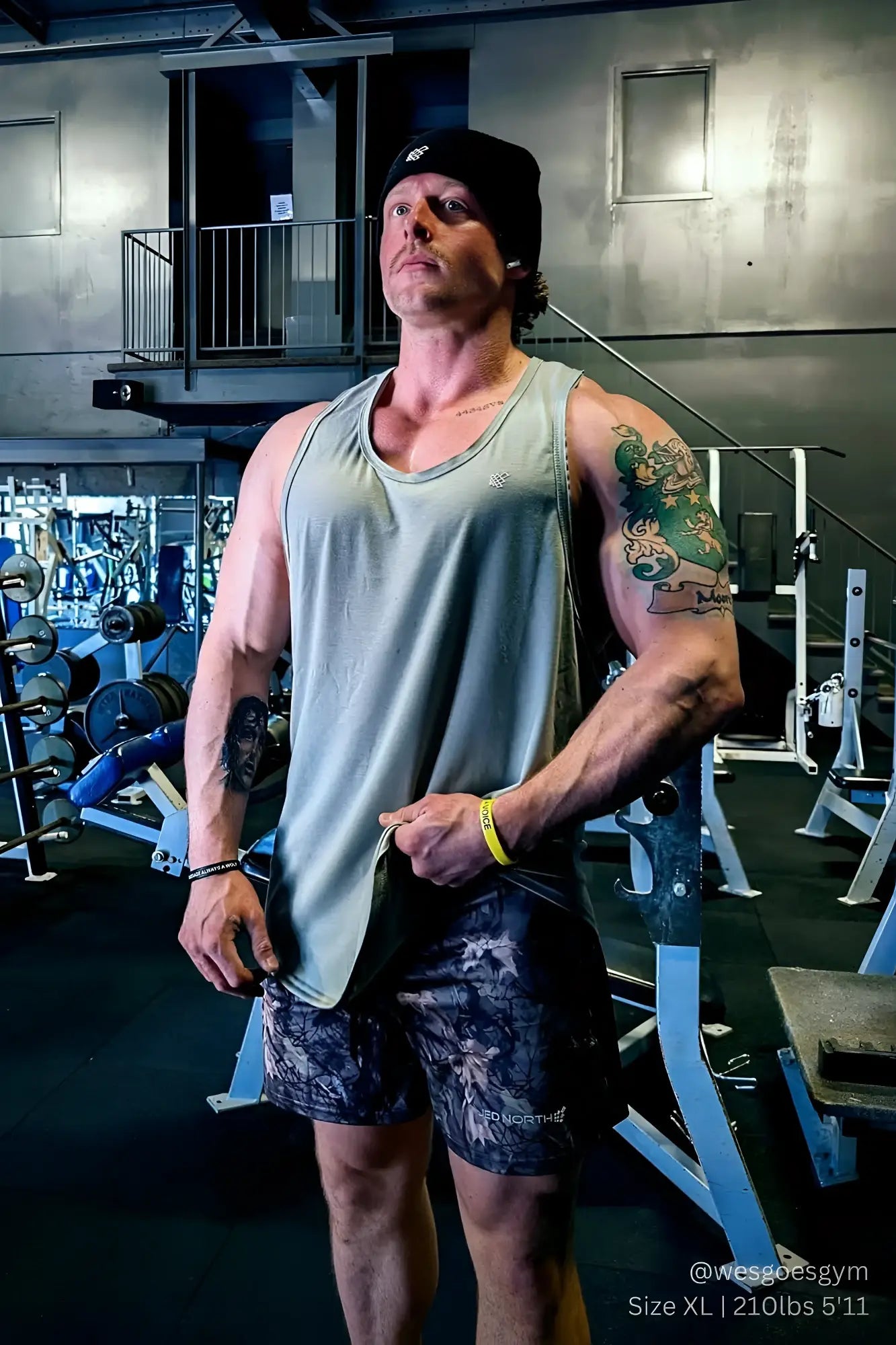 A muscular man wearing a gray jed north vital raw-hem tank top 2.0 made of light breathable fabric and dark patterned shorts