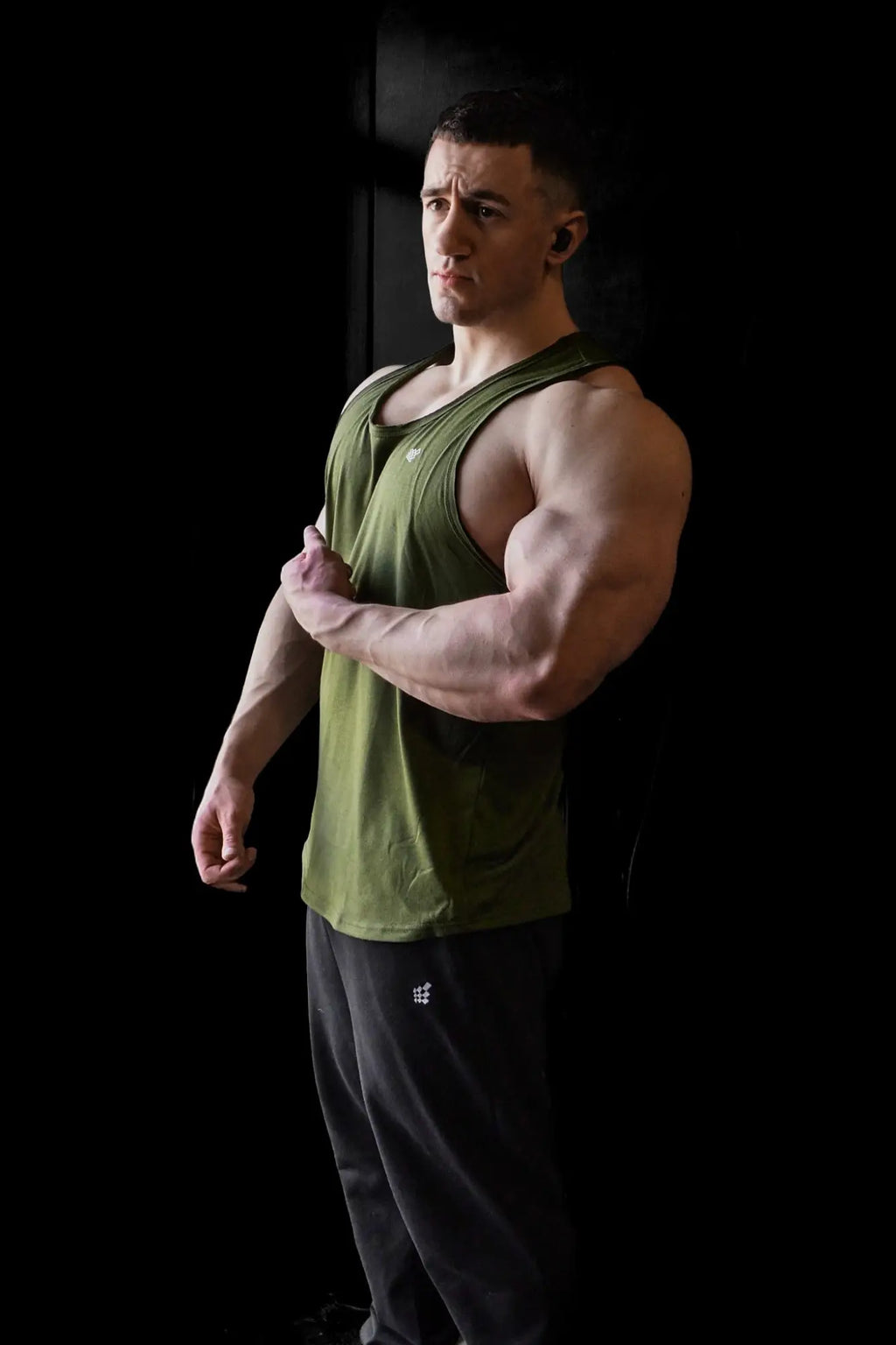 A man wearing a green Jed North Vital Raw-Hem Tank Top 2.0 paired with dark gray athletic pants