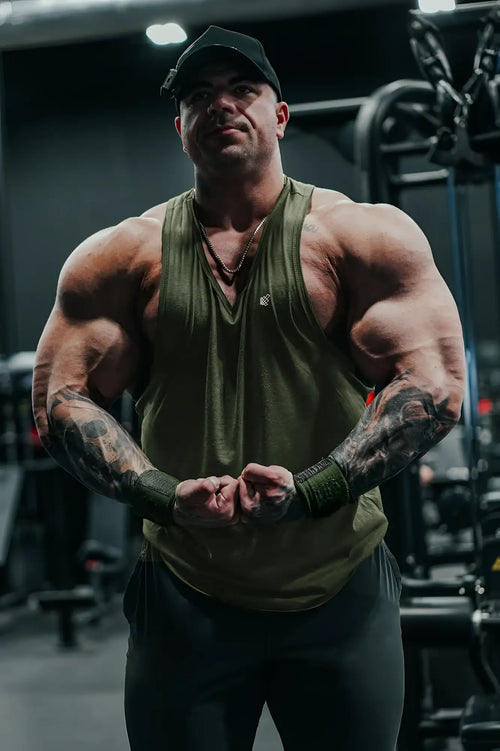 Muscular man wearing a green Jed North Vital Raw-Hem Tank Top 2.0 with black cap showcasing the front view