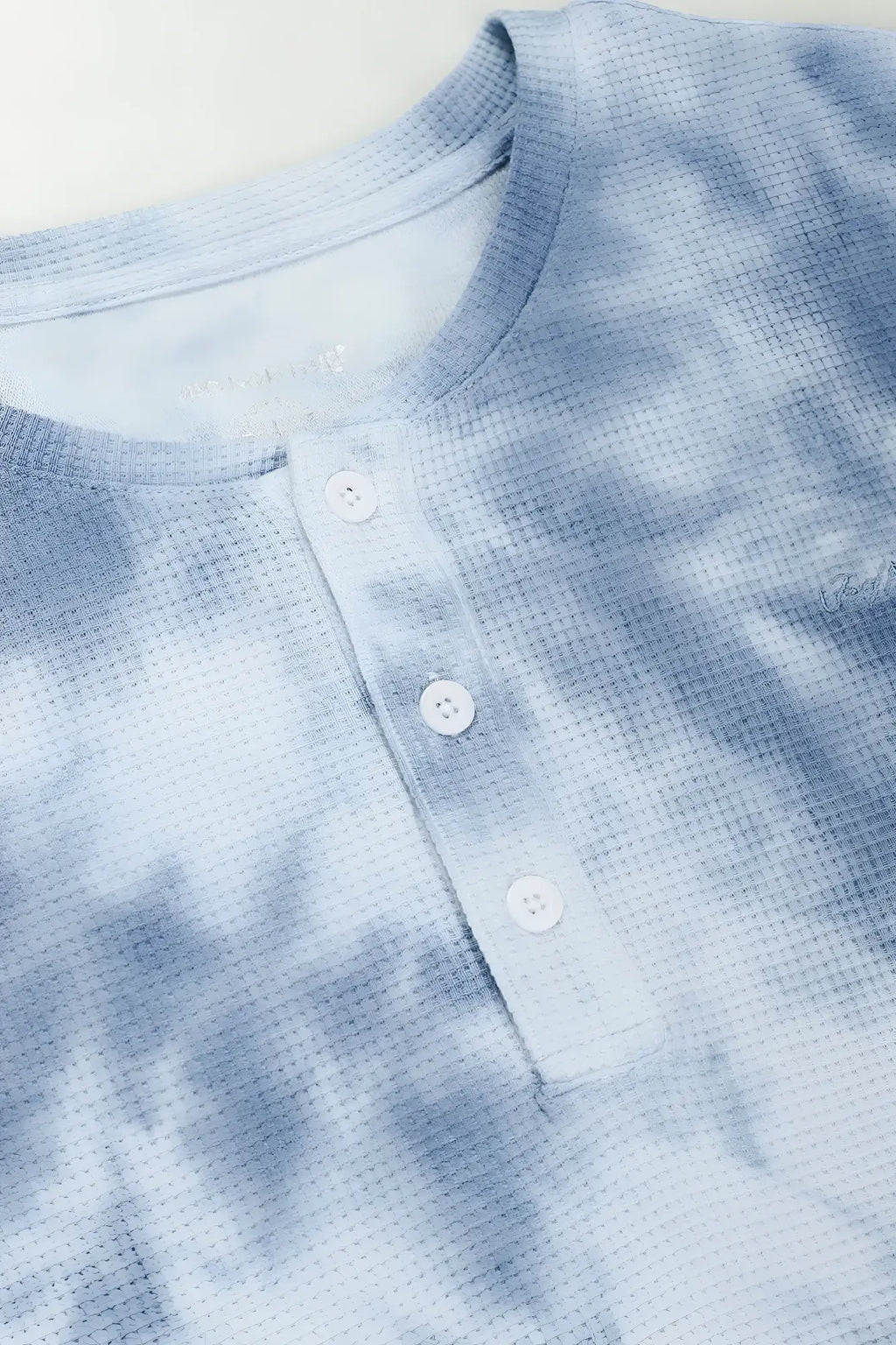 A light blue tie dye waffle henley t shirt with subtle textured weave and white buttons for casual wear