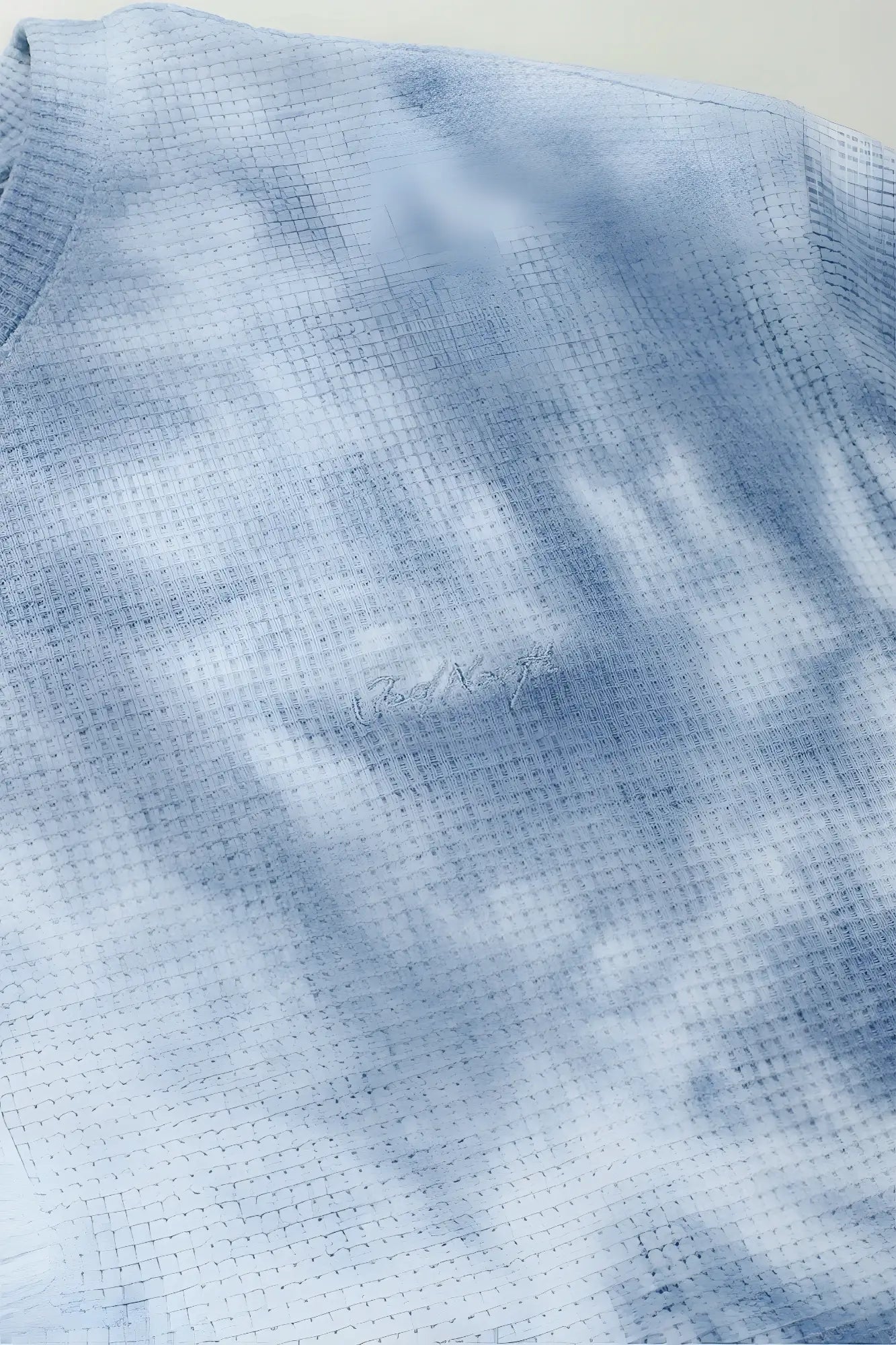 A light blue tie dye waffle henley t shirt with waffle knit texture and subtle embroidered logo on the chest