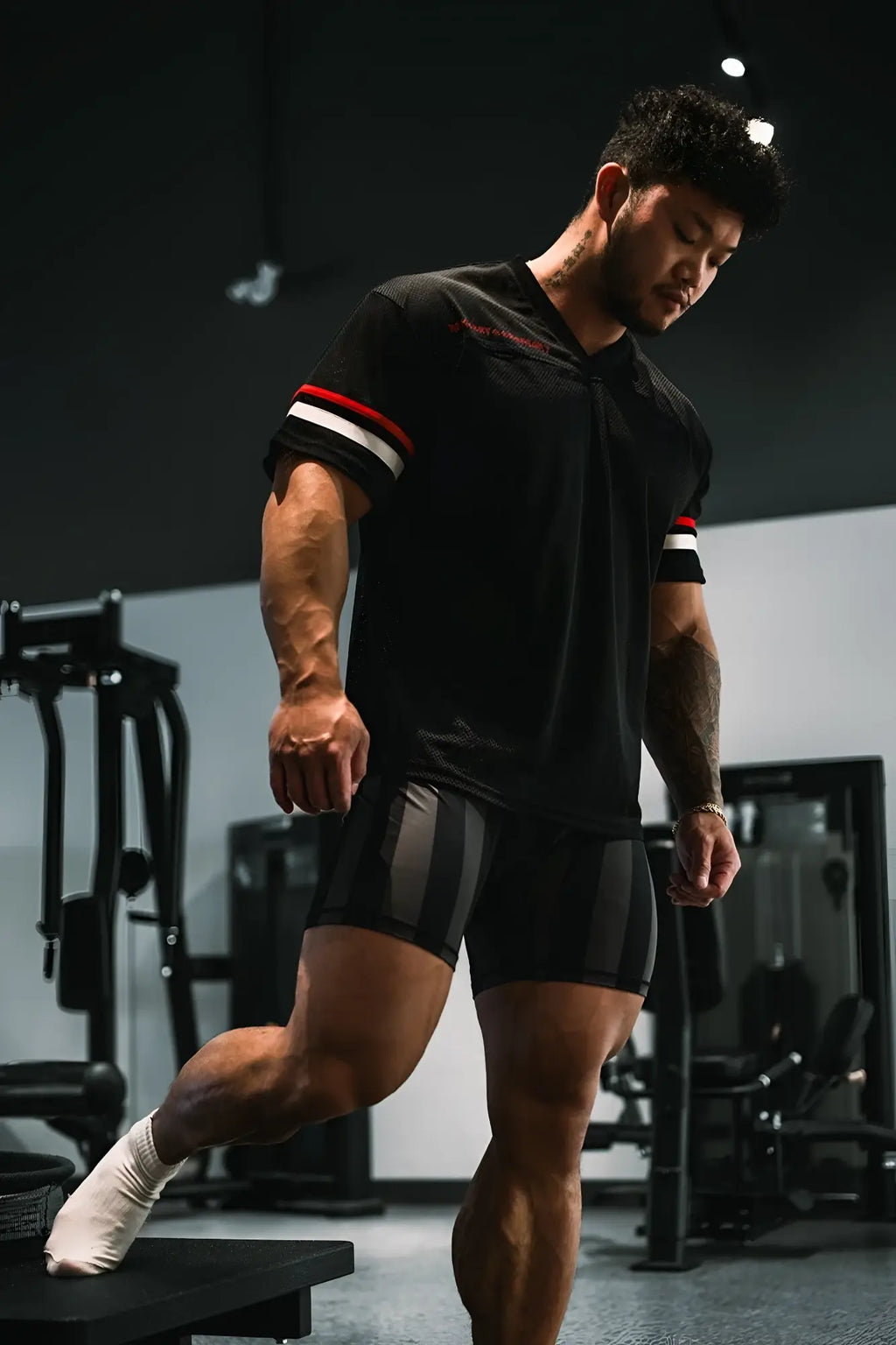 Muscular man wearing jed north warrior v-neck jersey black with red and white striped sleeves in gym setting