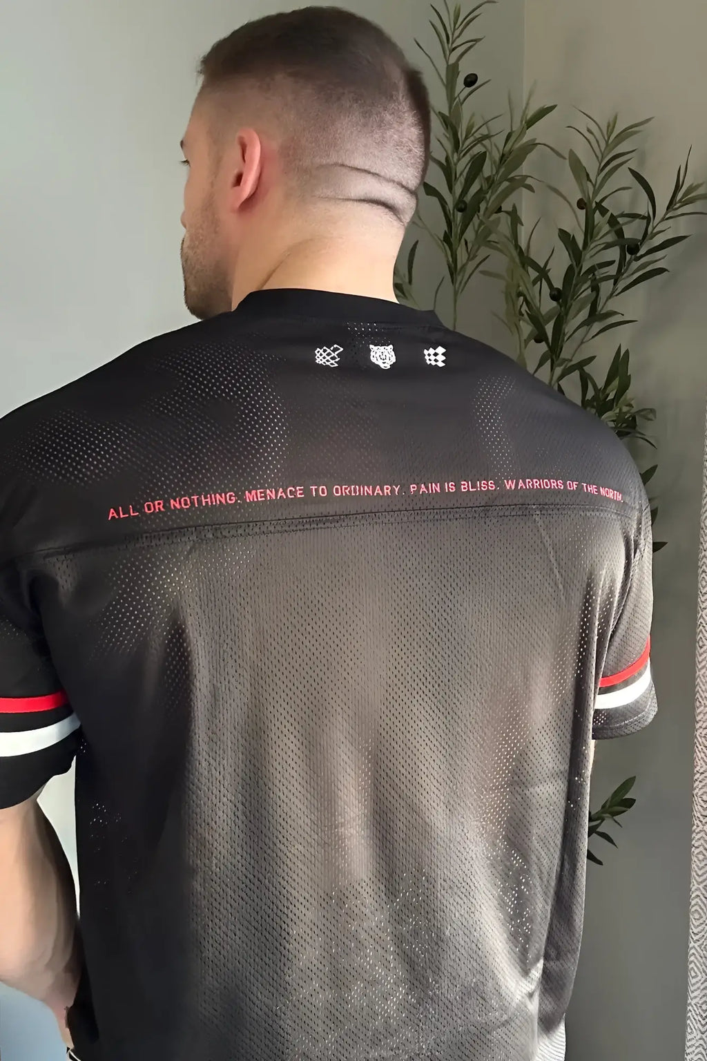 Back of jed north warrior v-neck jersey black with mesh texture and bold pink text trim in red and white on sleeves