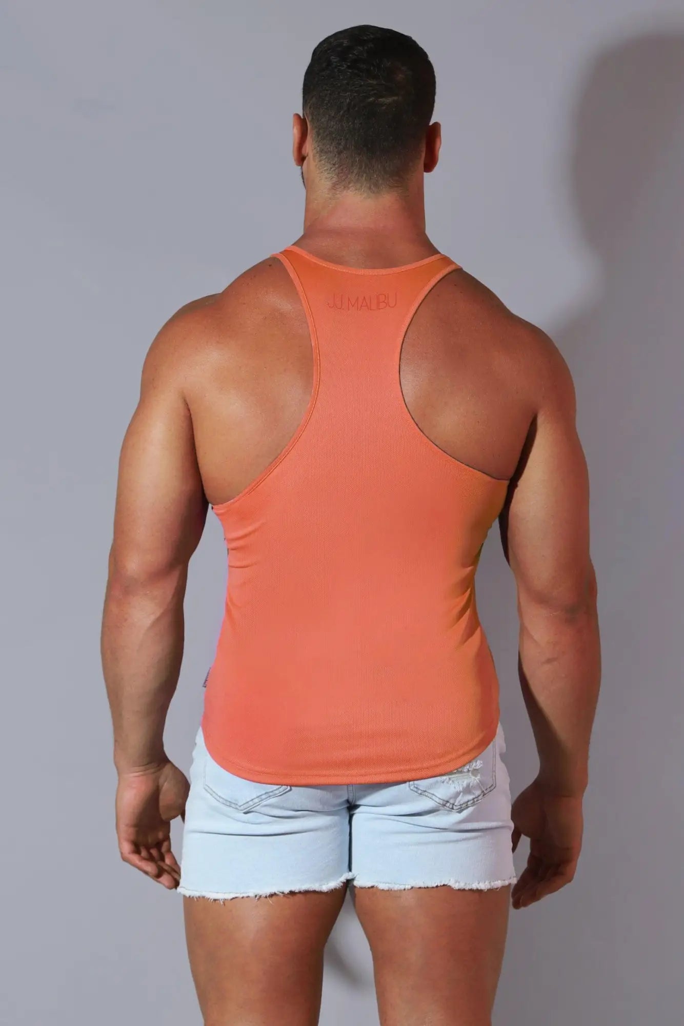 Orange racerback gym stringer tank top in cool-dry fabric with subtle brand logo at neckline coral color