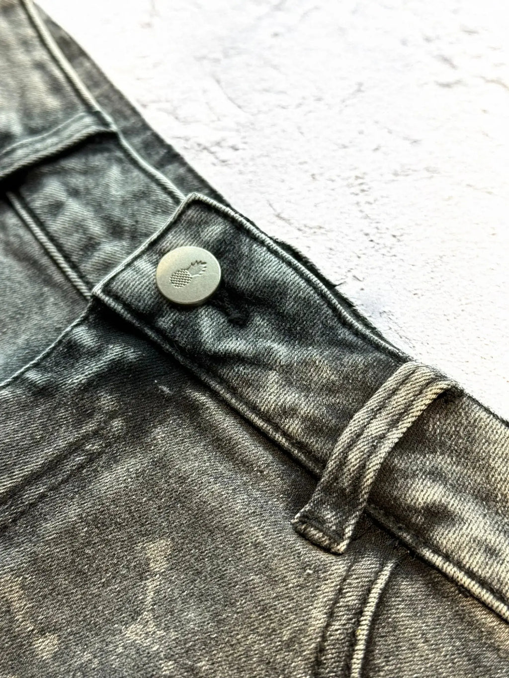 Acid washed distressed booty shorts in black dark gray denim with metallic button embossed pineapple logo back view
