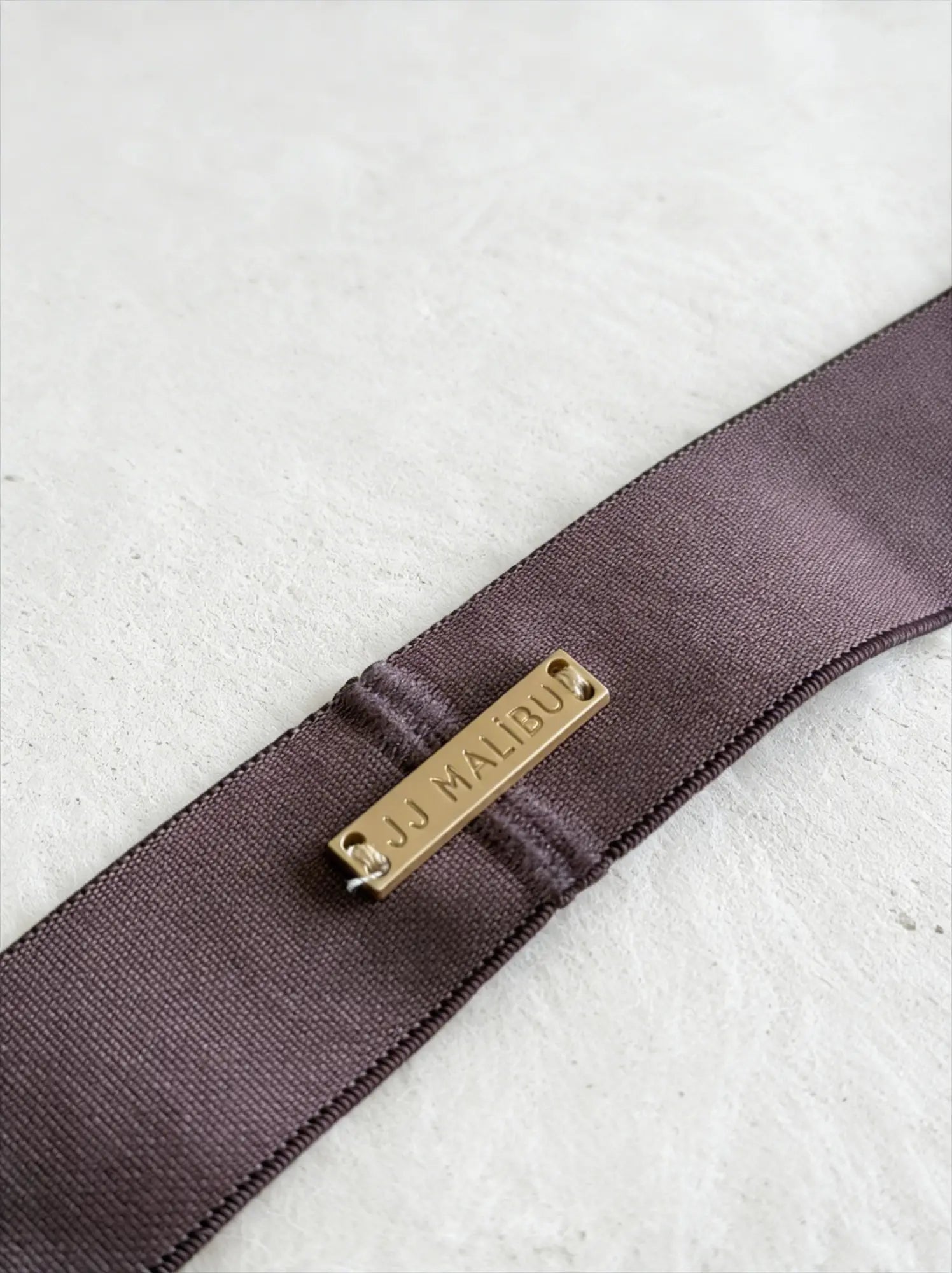 A sleek taupe on-display jockstrap with a dark purple satin belt strap and gold-tone jj malibu metal plaque