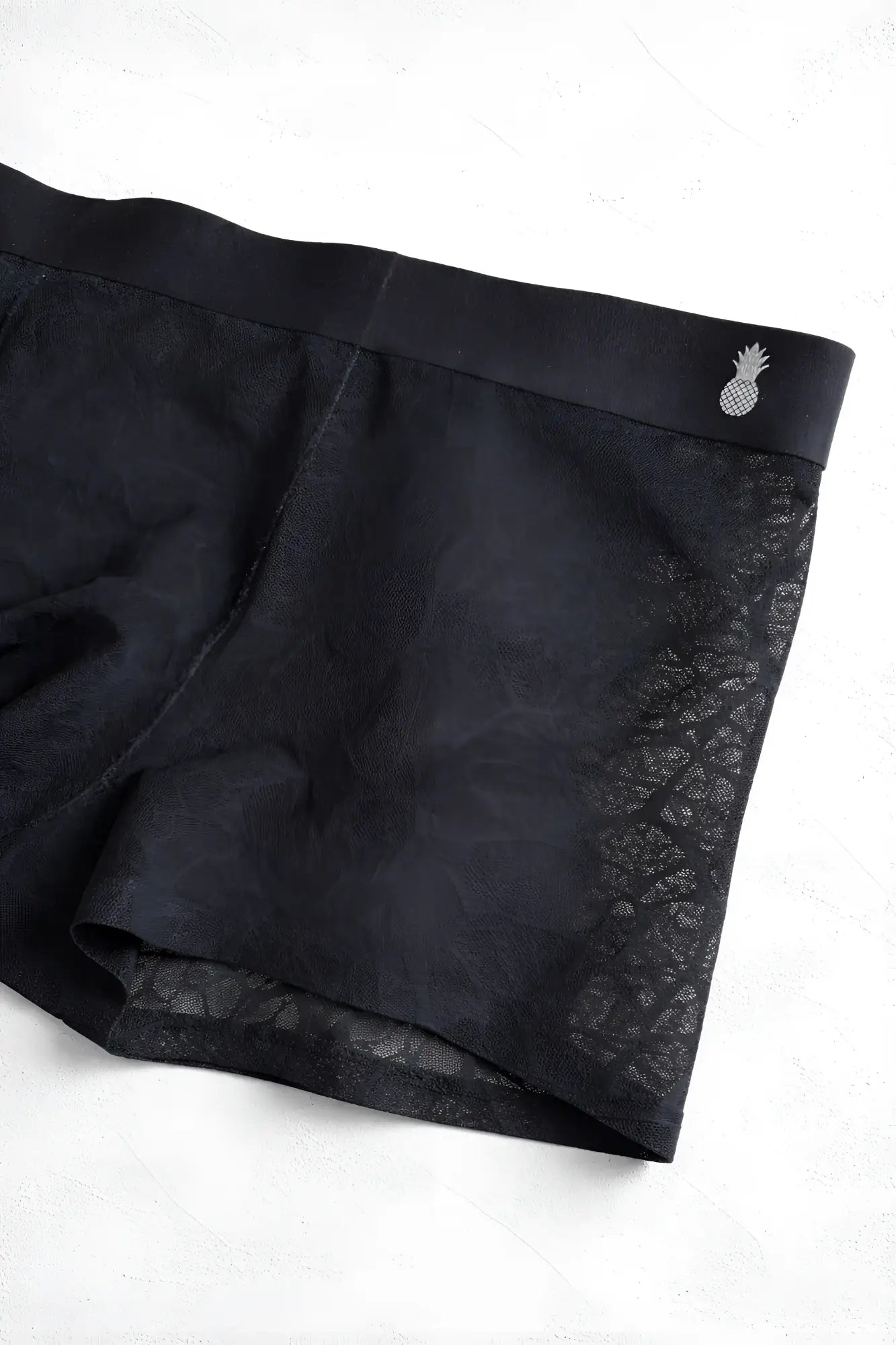 Charcoal black geo-mesh seamless boxers with subtle textured lace pattern and silver pineapple emblem on waistband