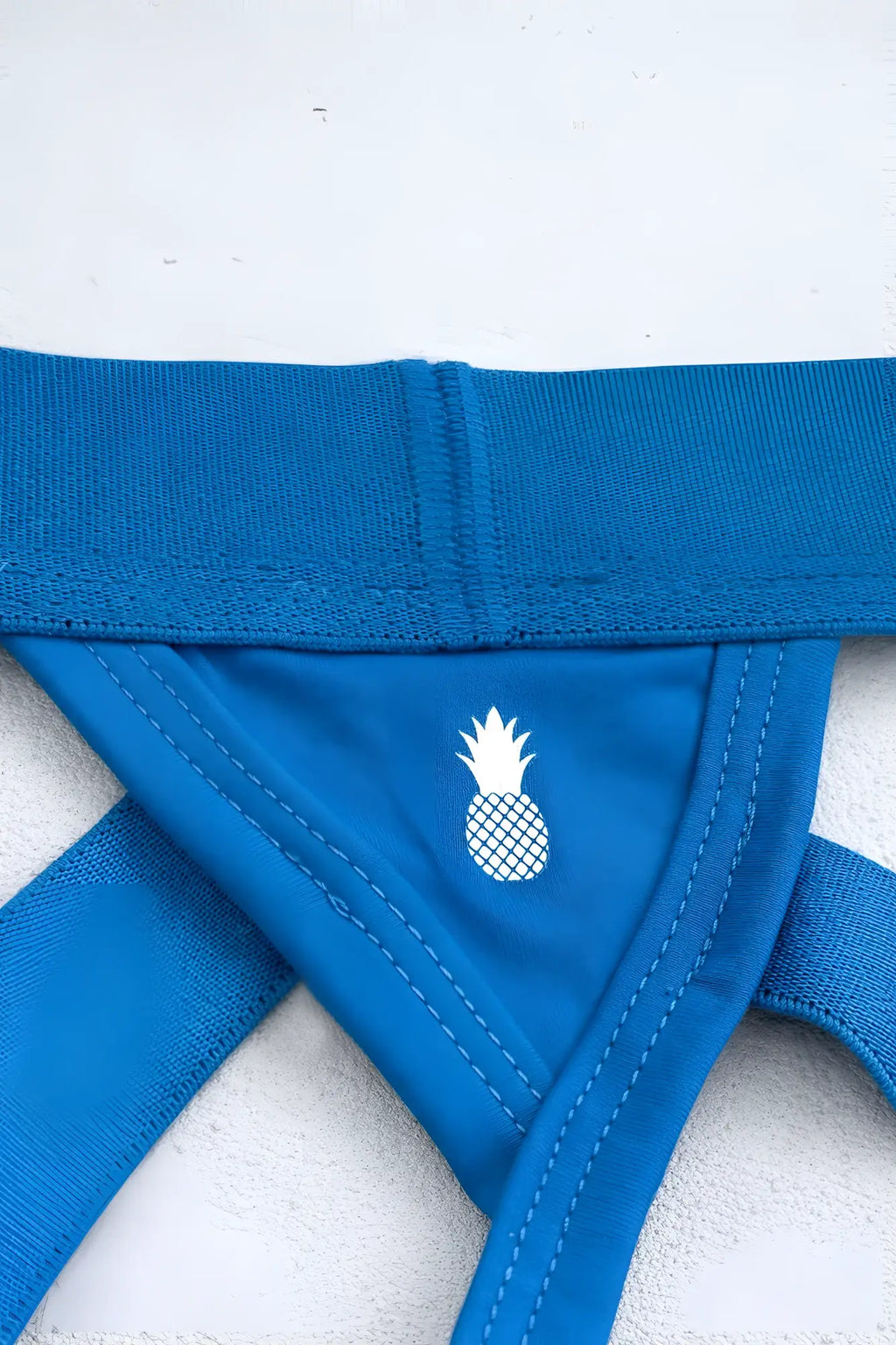 Blue pineapple-themed bikini bottom with white embroidered logo and elastic straps shown from the back for travel use
