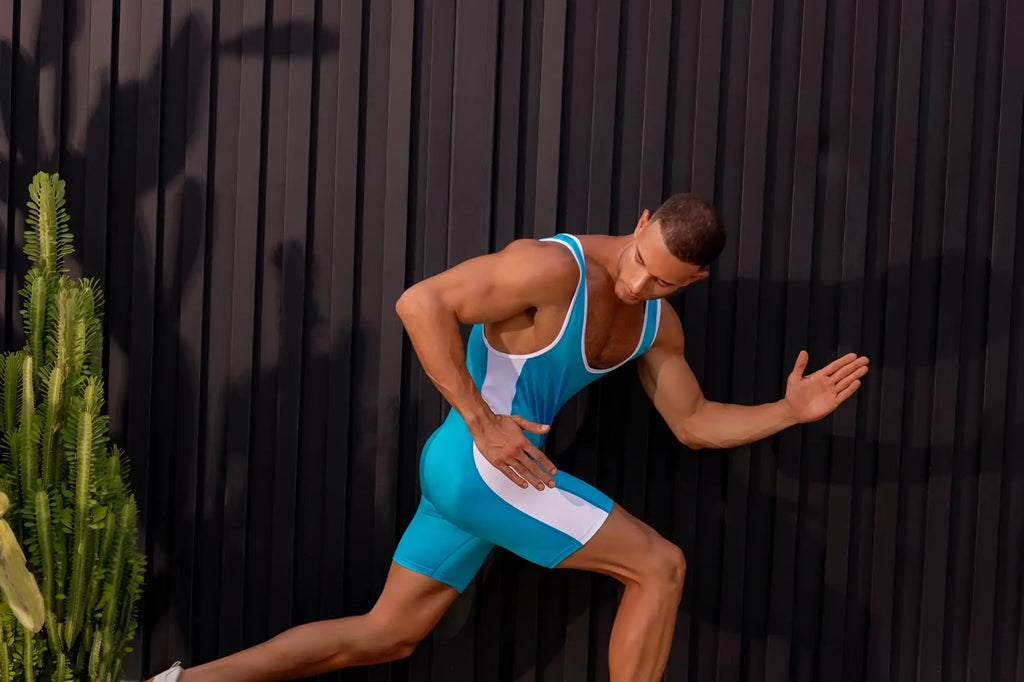 A muscular man wearing a turquoise JOR 2216 fighter bodysuit with sleek seamless athletic singlet material