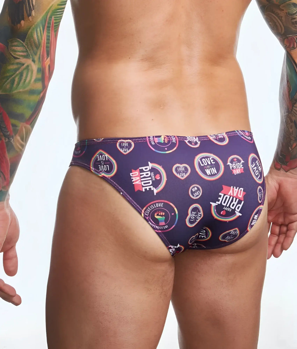 Purple swim trunks by justin simon featuring vibrant rainbow pride day logos and text in a classic mens bikini style