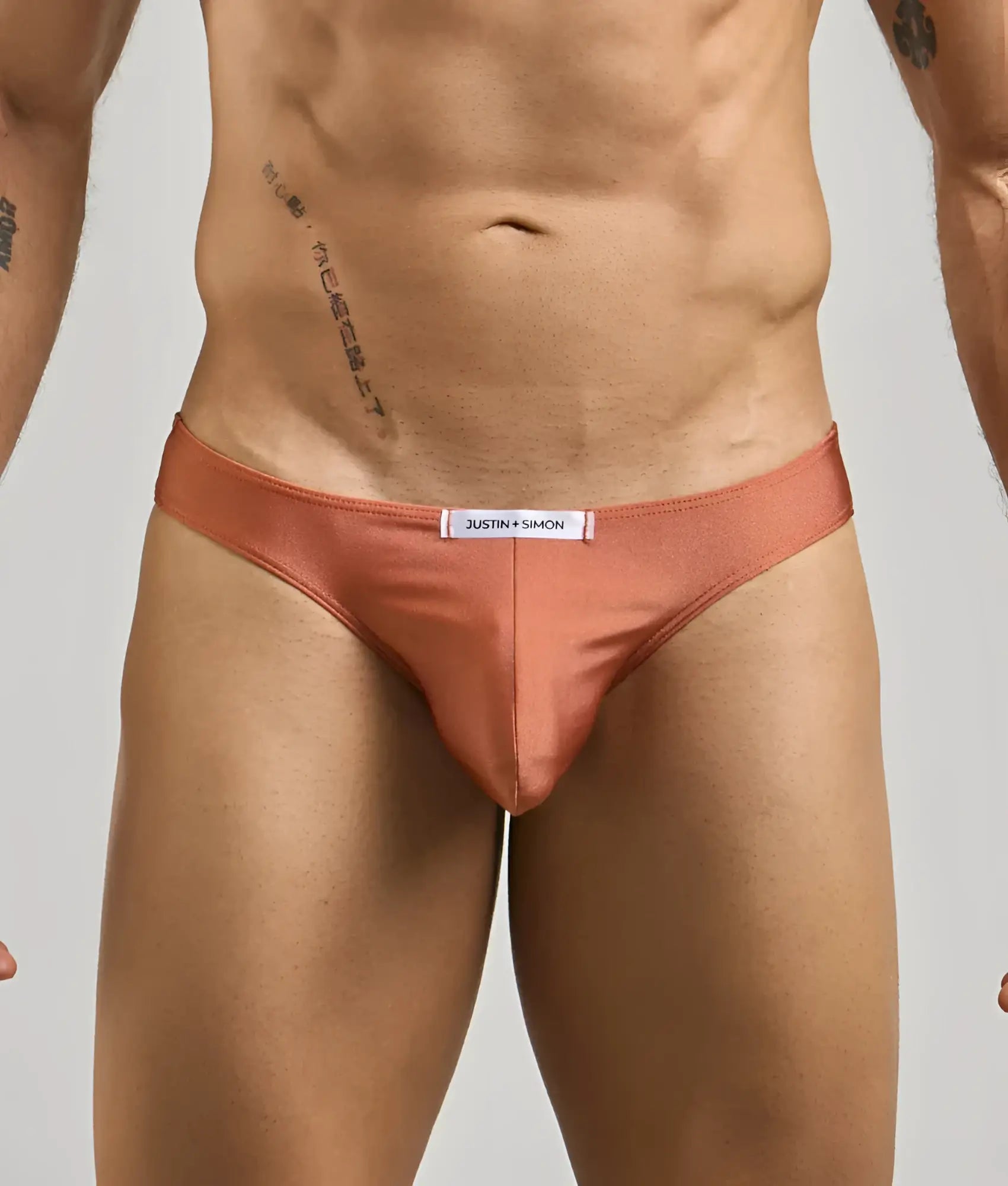 Coral-colored satin briefs with a white justin + simon label at the waistband from the classic mens bikini line